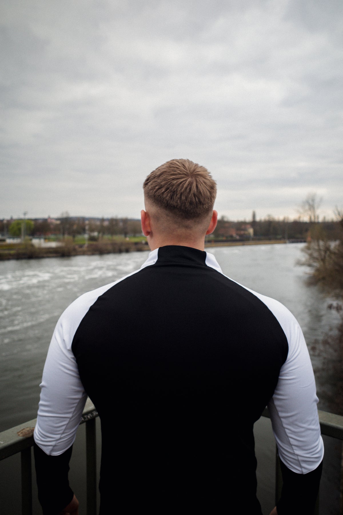 Rückansicht schwarzer Halfzip-Sweater mit weißem Ärmel am Flussufer
