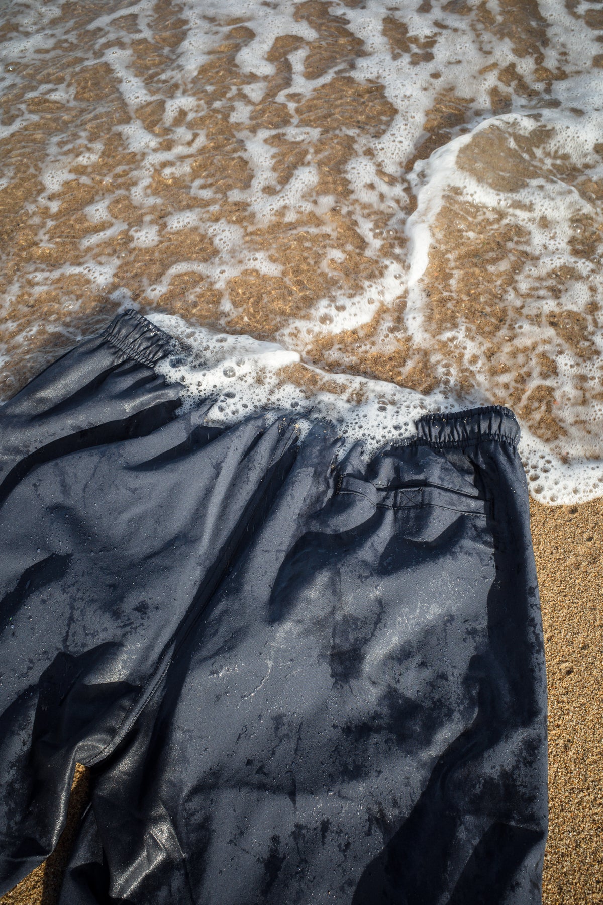 Wet navy swim trunks flat lay on beach sand
