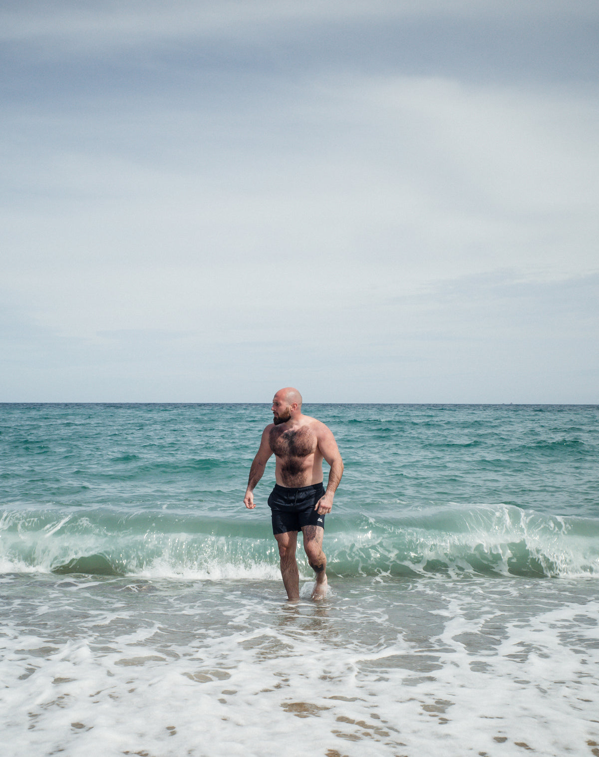 Man walking out of ocean in navy swim trunks