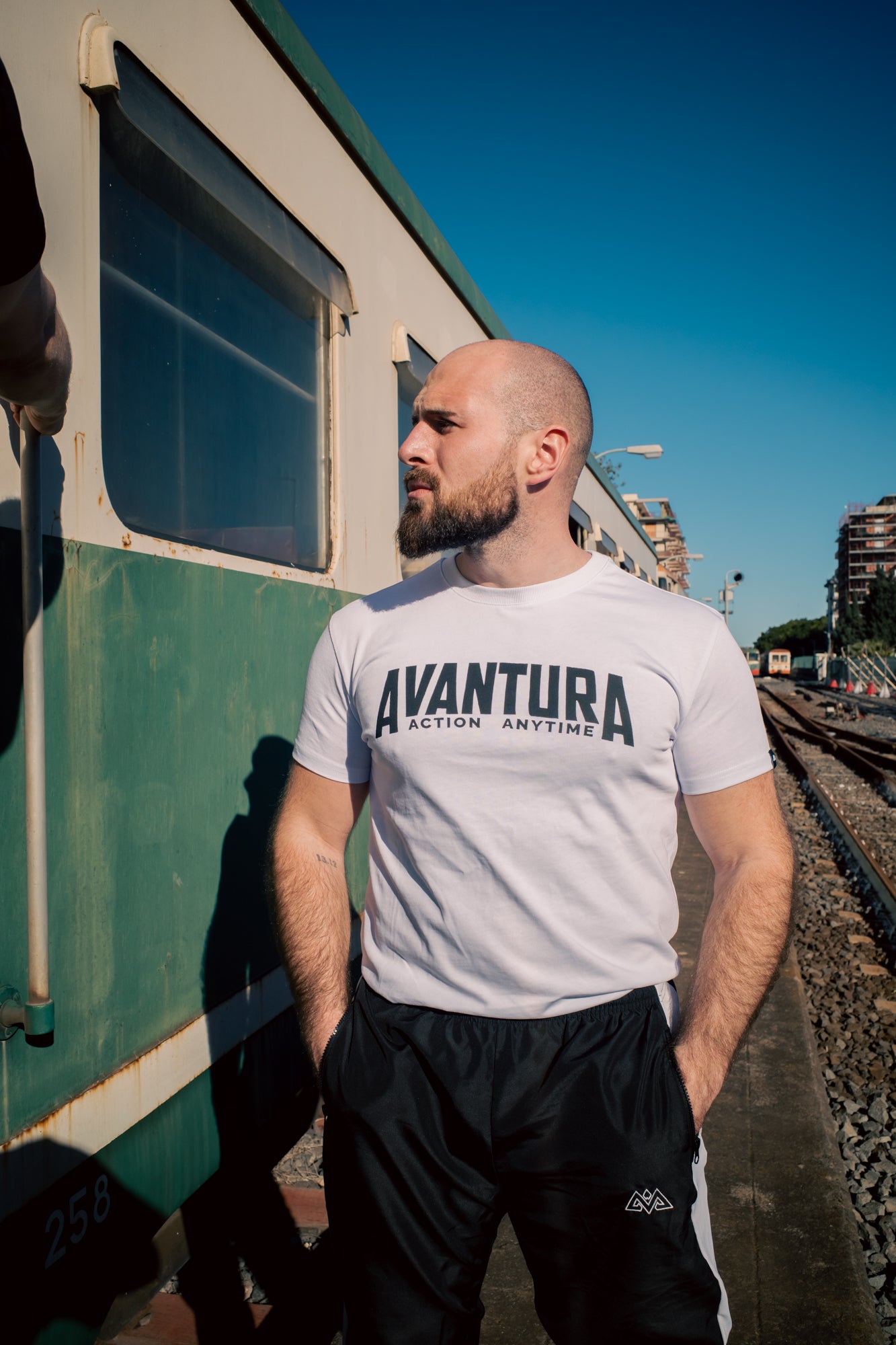 Man wearing white Avantura T-shirt and black track pants on train platform