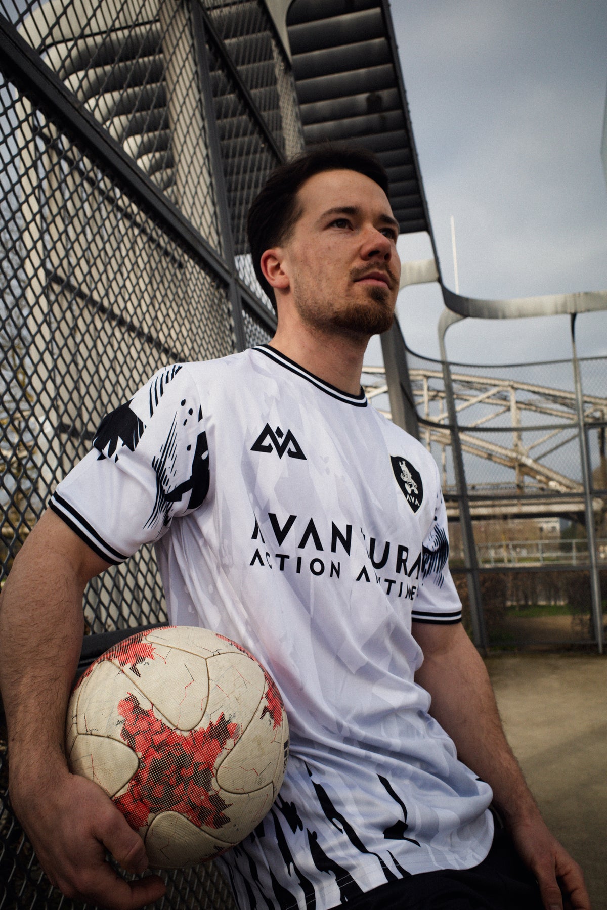 White Avantura jersey with black abstract graphics and 'Action Anytime' text, worn by athlete holding soccer ball