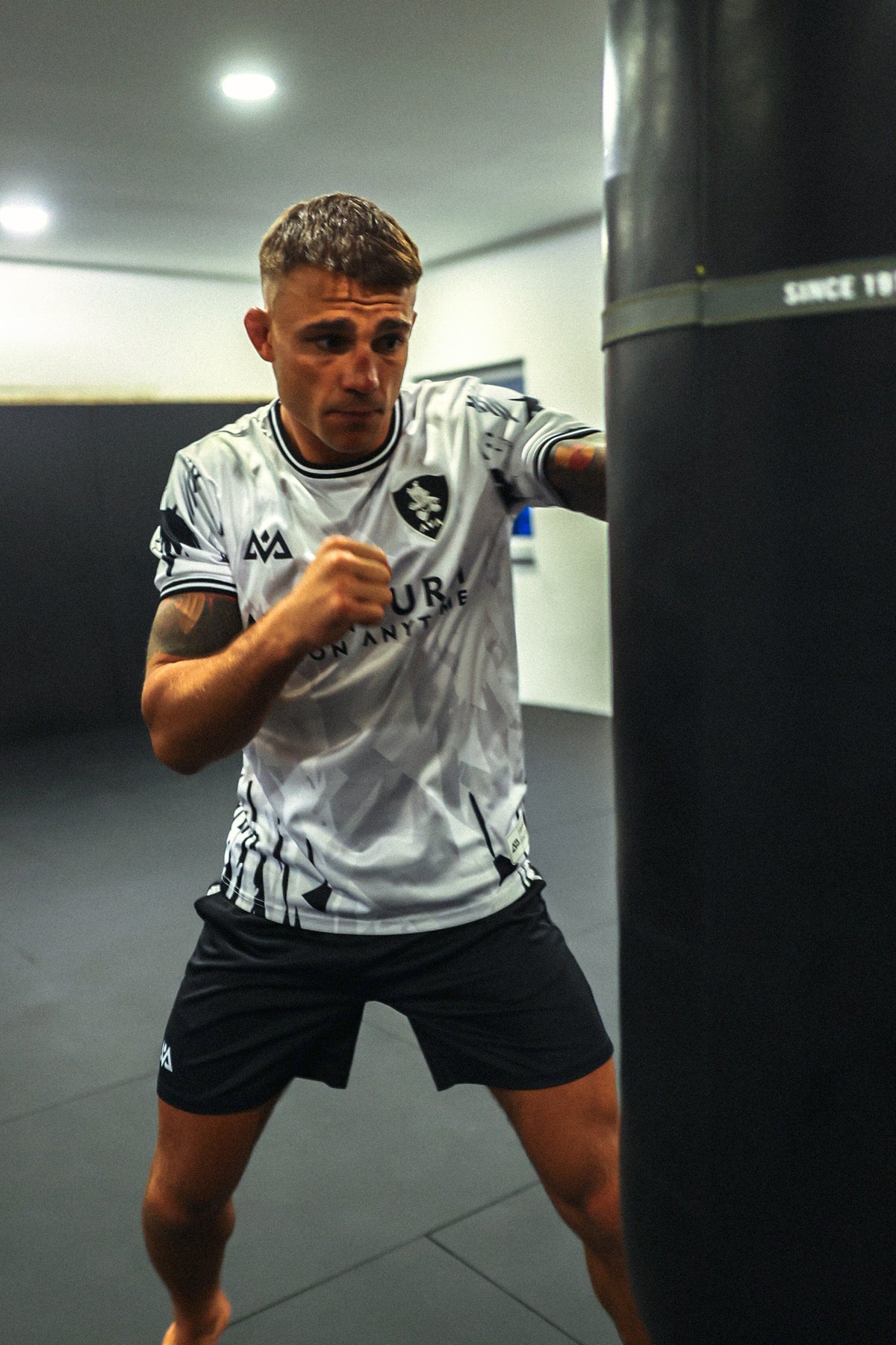 Man in white Avantura jersey practicing boxing stance with punching bag in gym setting