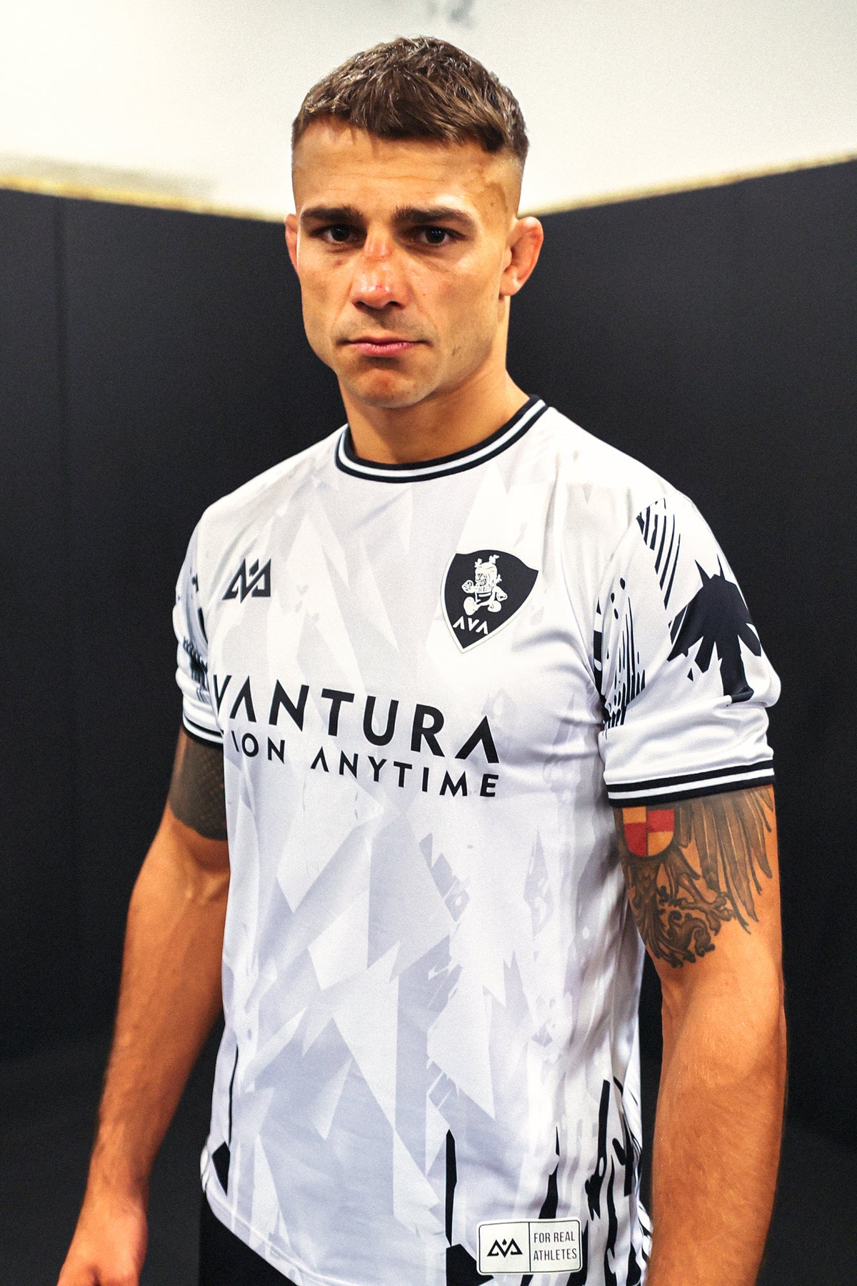 Front detail of white Avantura jersey showing shield logo patch and 'On Anytime' chest text