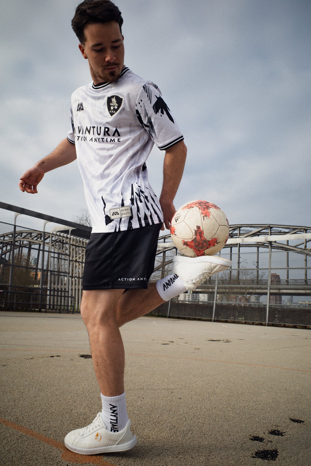 Athlete balancing soccer ball on knee wearing white Avantura jersey kit on concrete sports court
