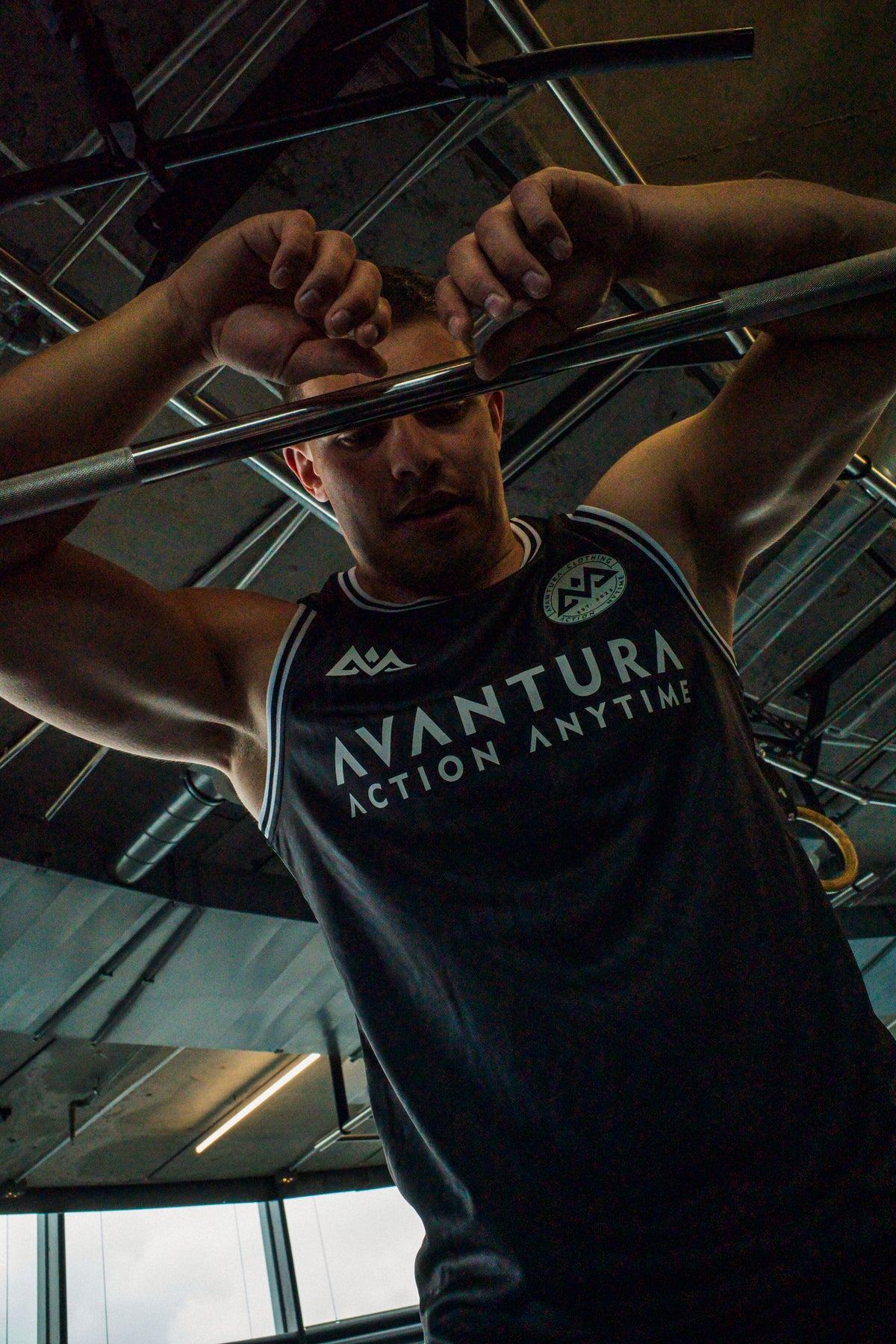 Man lifting barbell in black Avantura tank top with white chest graphics