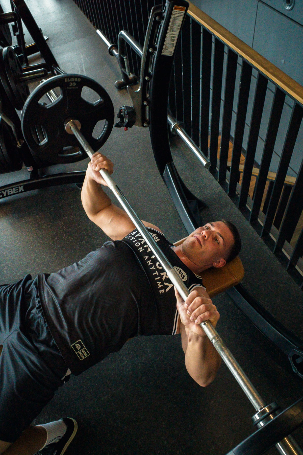 Bench press in black Avantura tank top showing woven label on lower hem