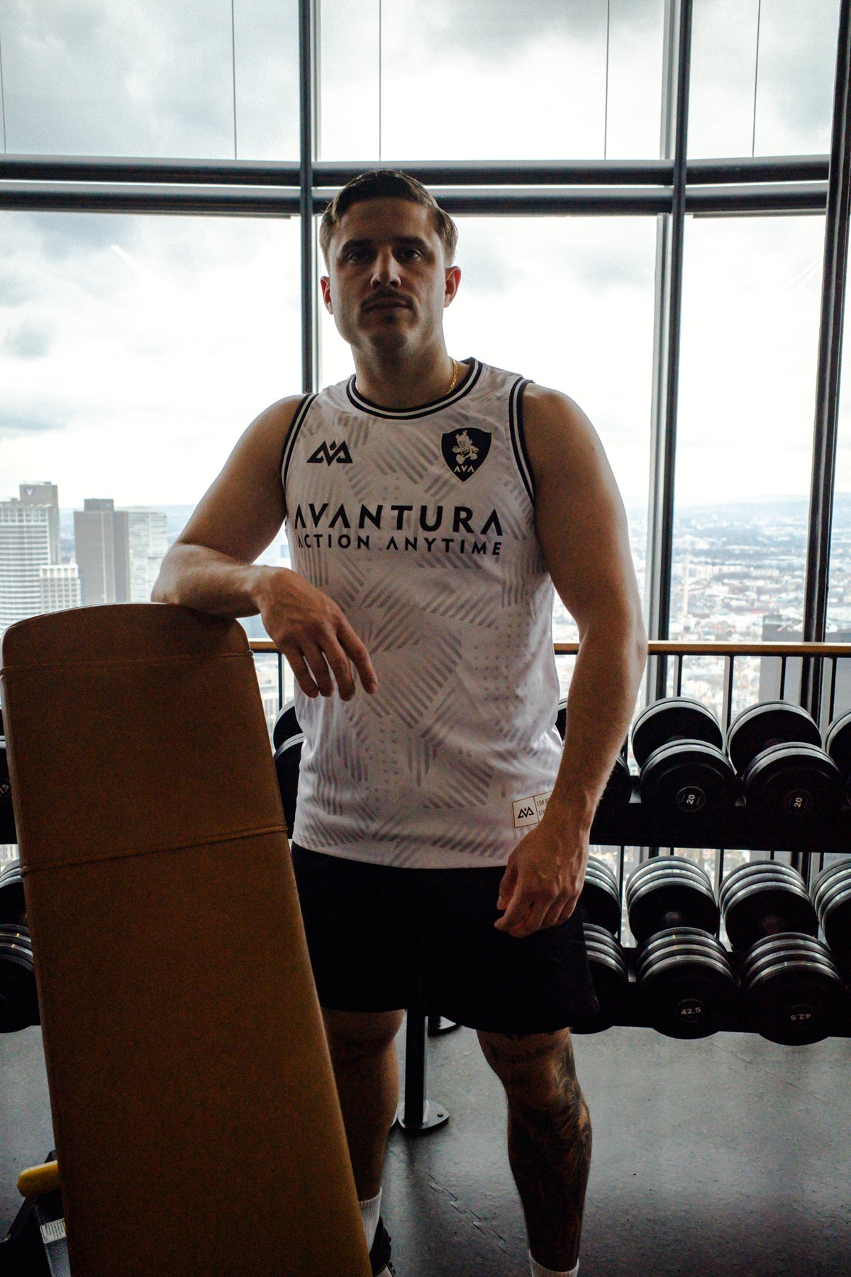 Man wearing white Avantura tank top with black trim leaning on bench