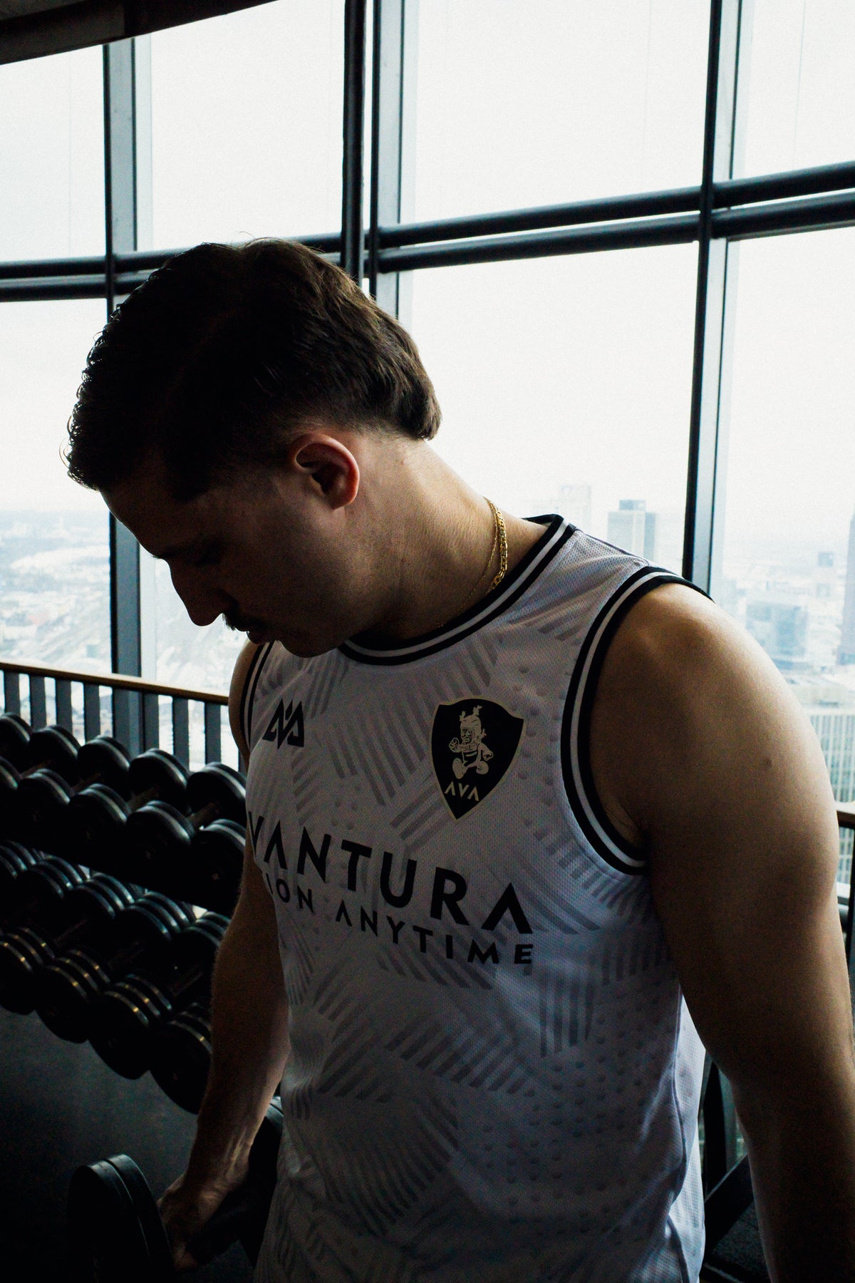 Side profile of man in white Avantura athletic tank top holding dumbbell