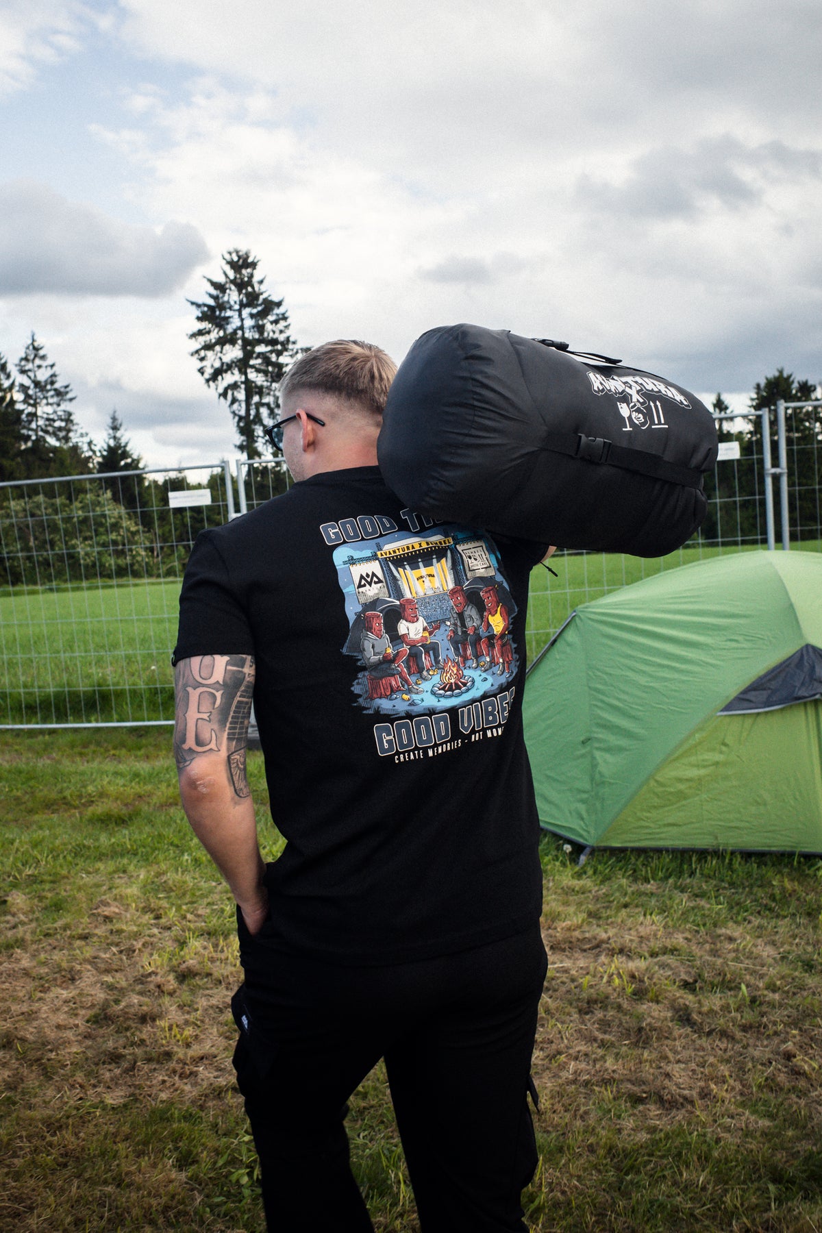 Man wearing black Avantura T-shirt with large back graphic carrying branded stuff sack