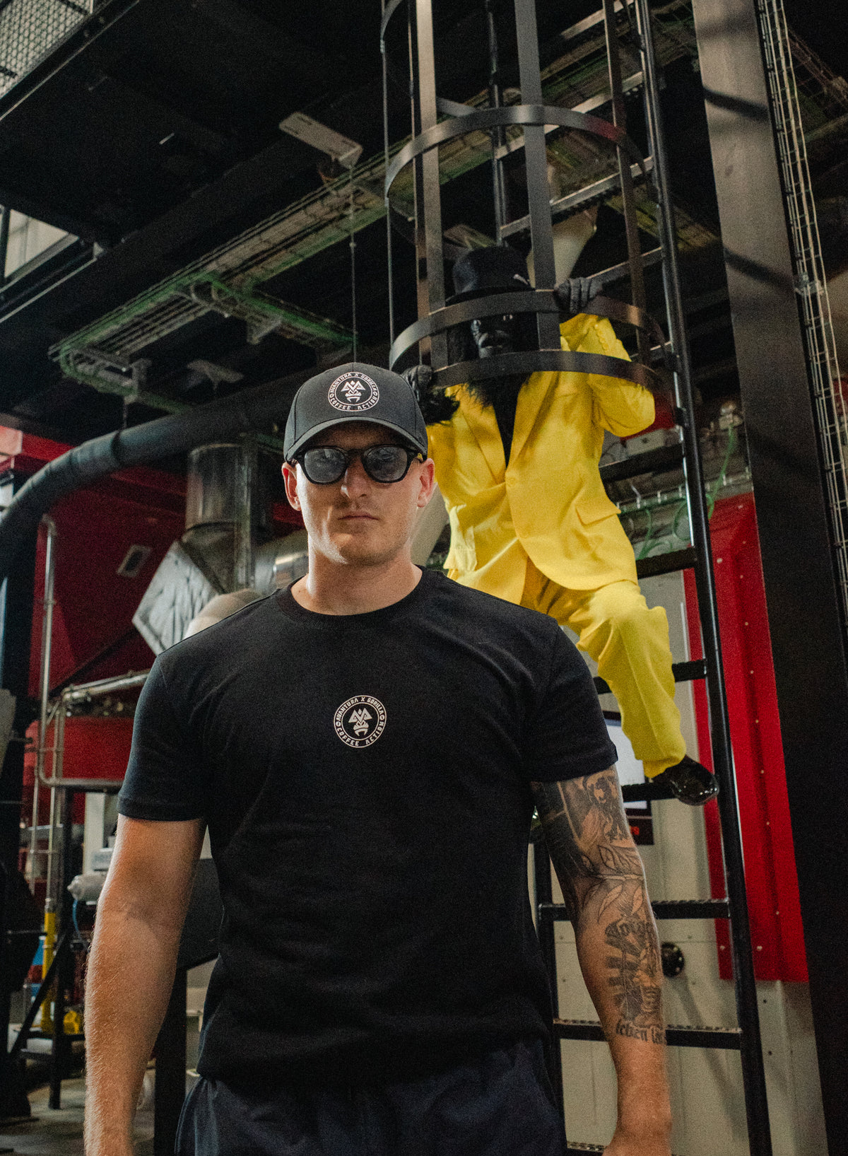 Man wearing black t-shirt with chest logo and cap climbing industrial structure