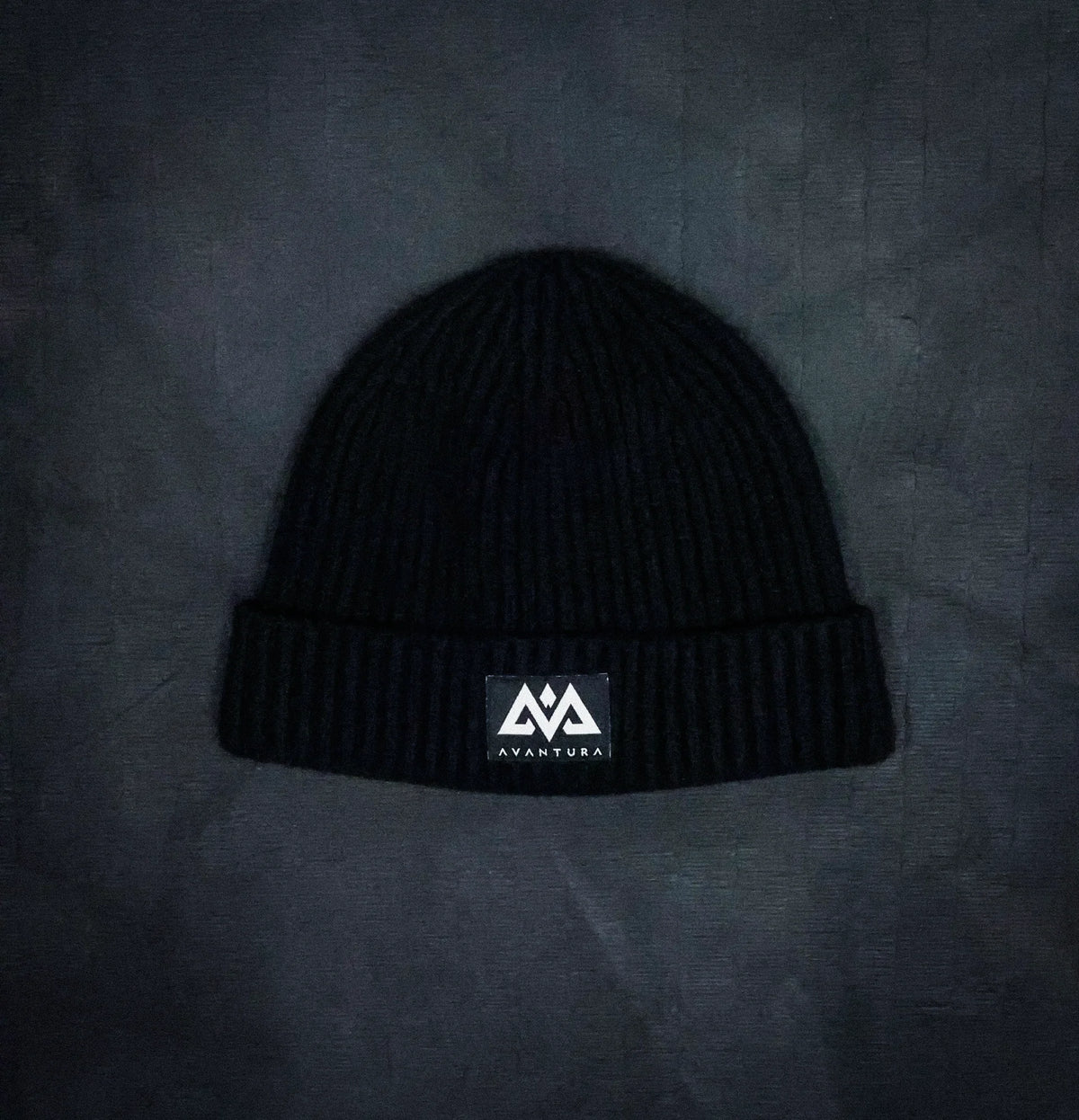 Flat lay of black ribbed knit beanie showing textured fabric and patch