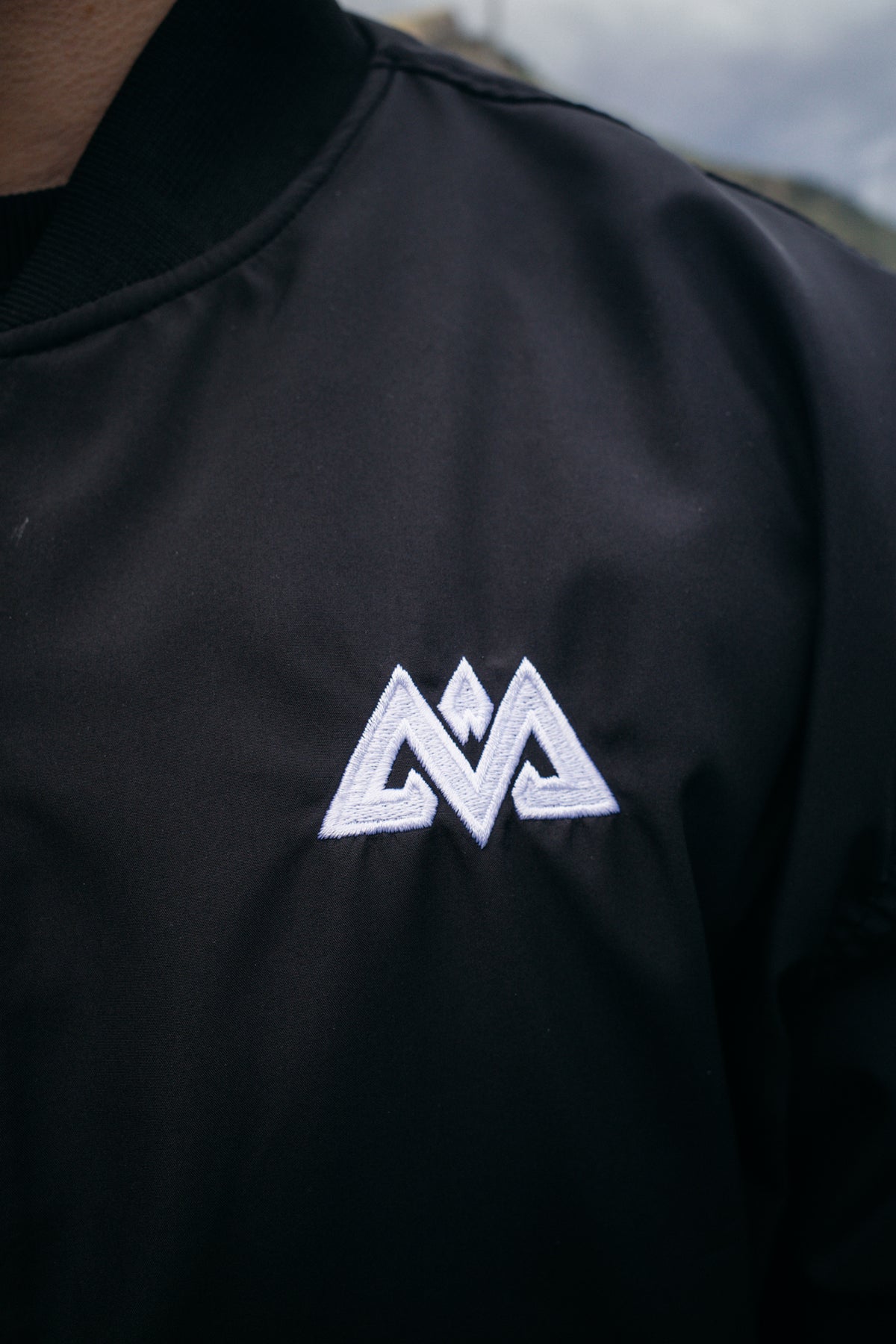 White embroidered geometric logo on black bomber jacket