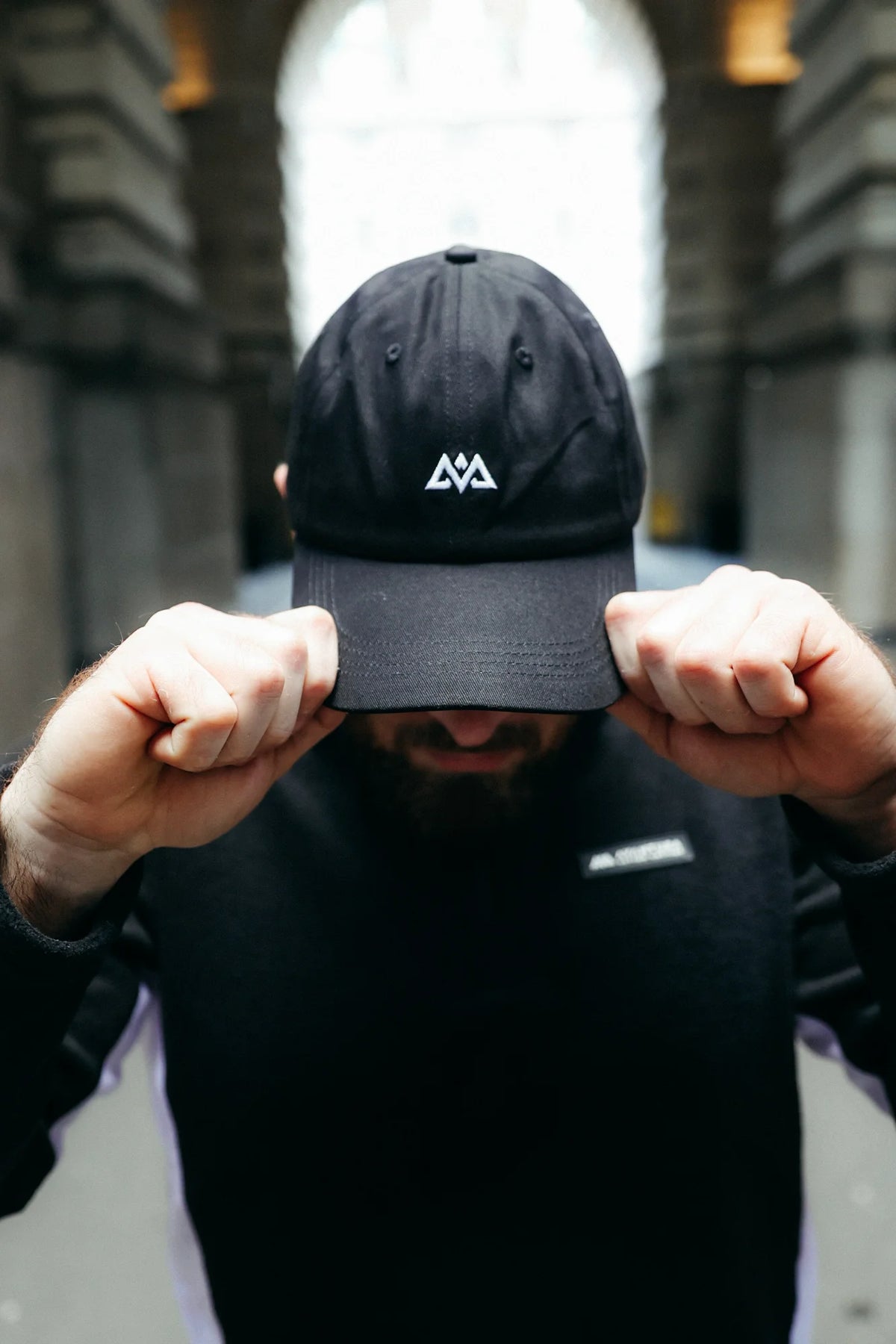 Black Avantura baseball cap with white logo, worn by man in architectural setting