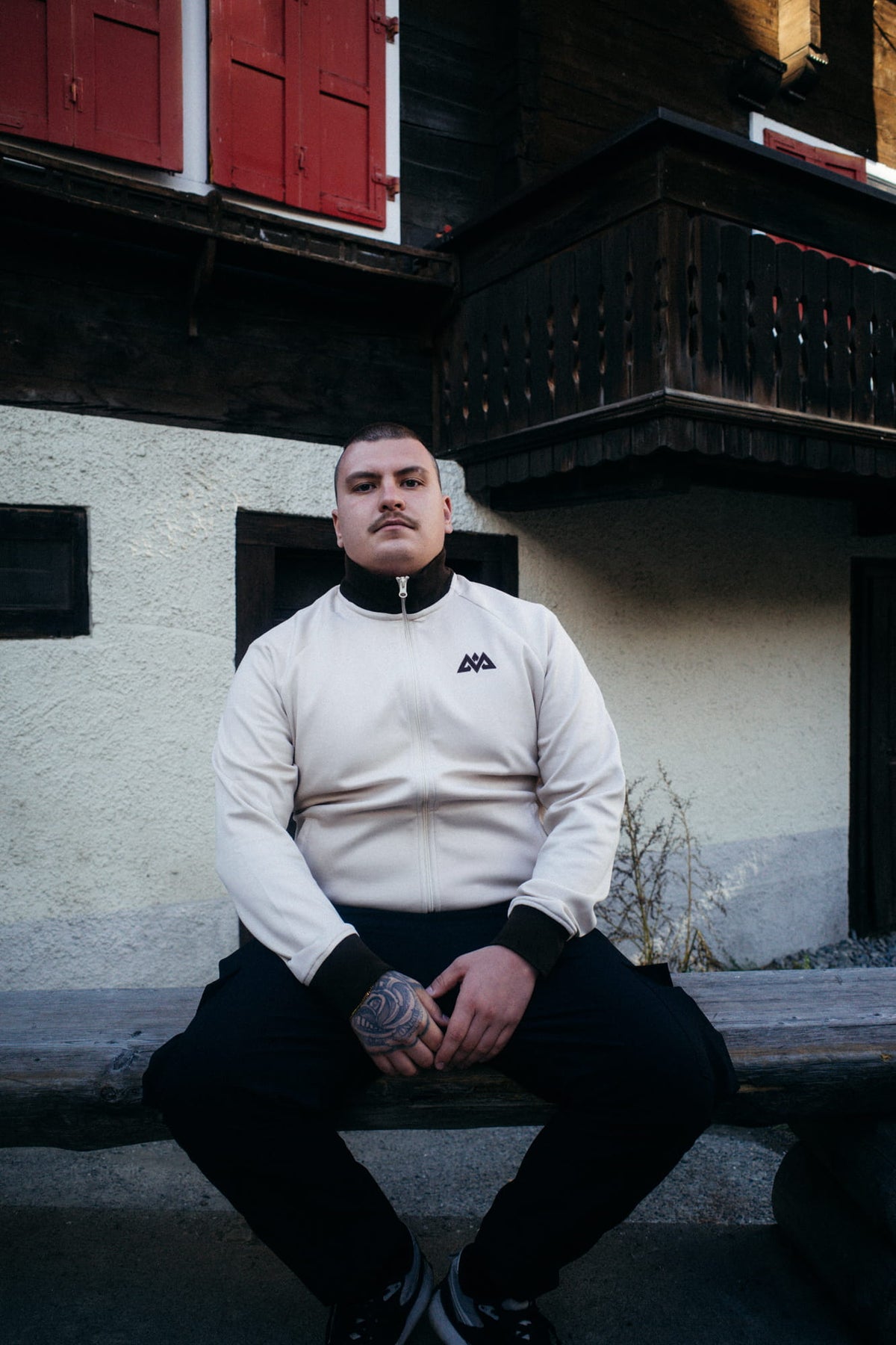 Mann sitzt in geschlossener cremefarbener Trackjacke