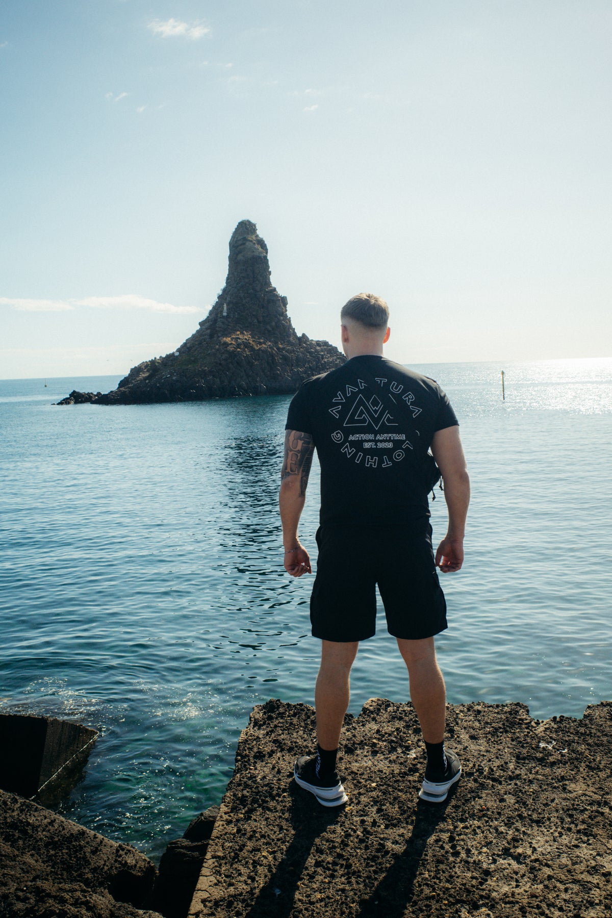 Man in black logo T-shirt at rocky coast