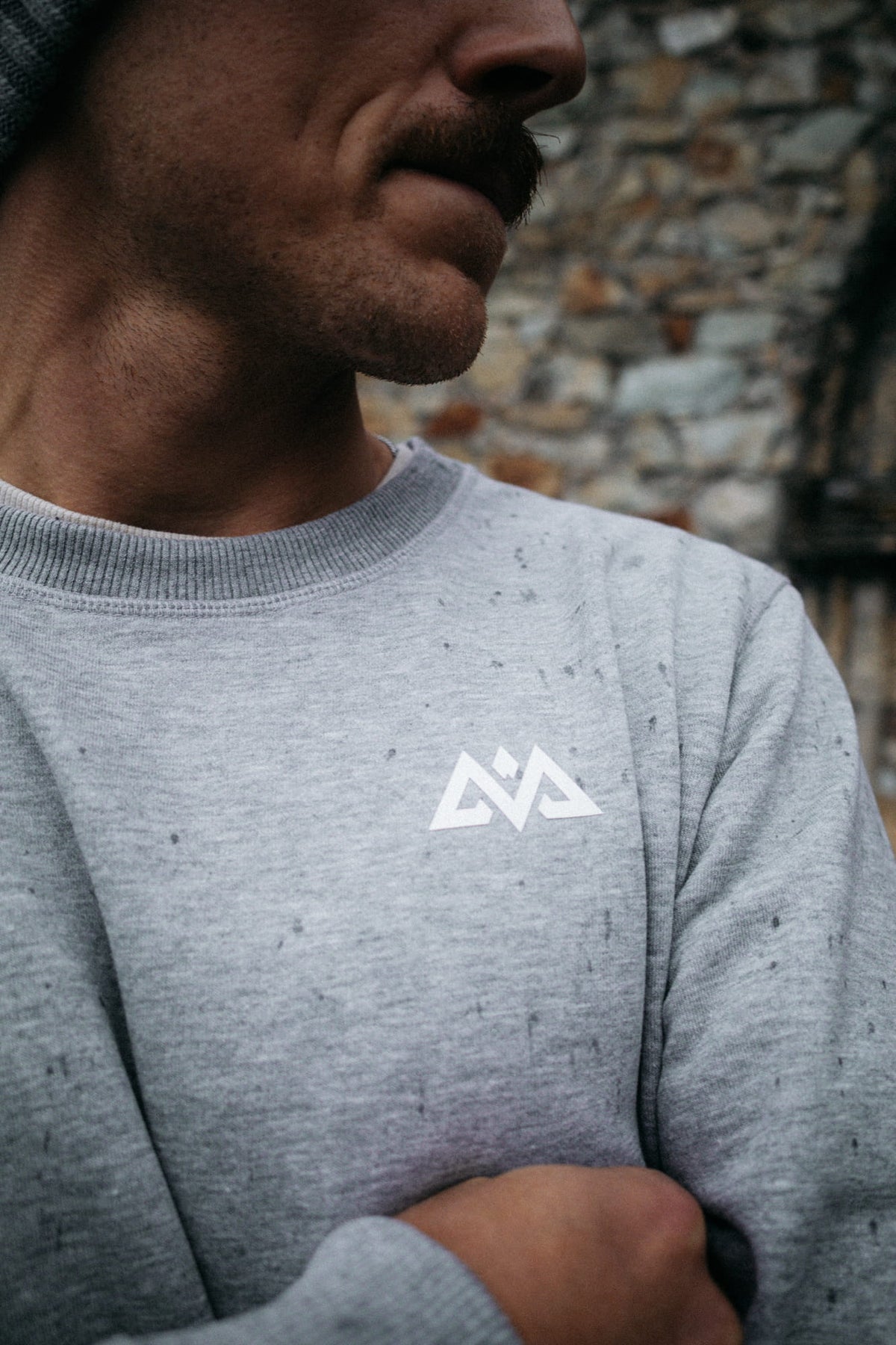 Detailansicht des weißen Logos und der melierten Stoffstruktur am Sweatshirt