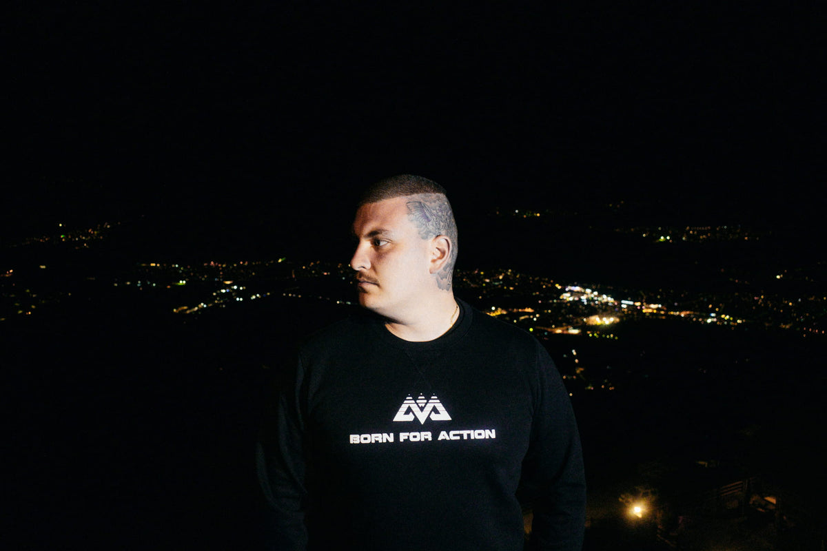 Schwarzer Pullover mit geometrischem Logo und BORN FOR ACTION Text bei Nacht