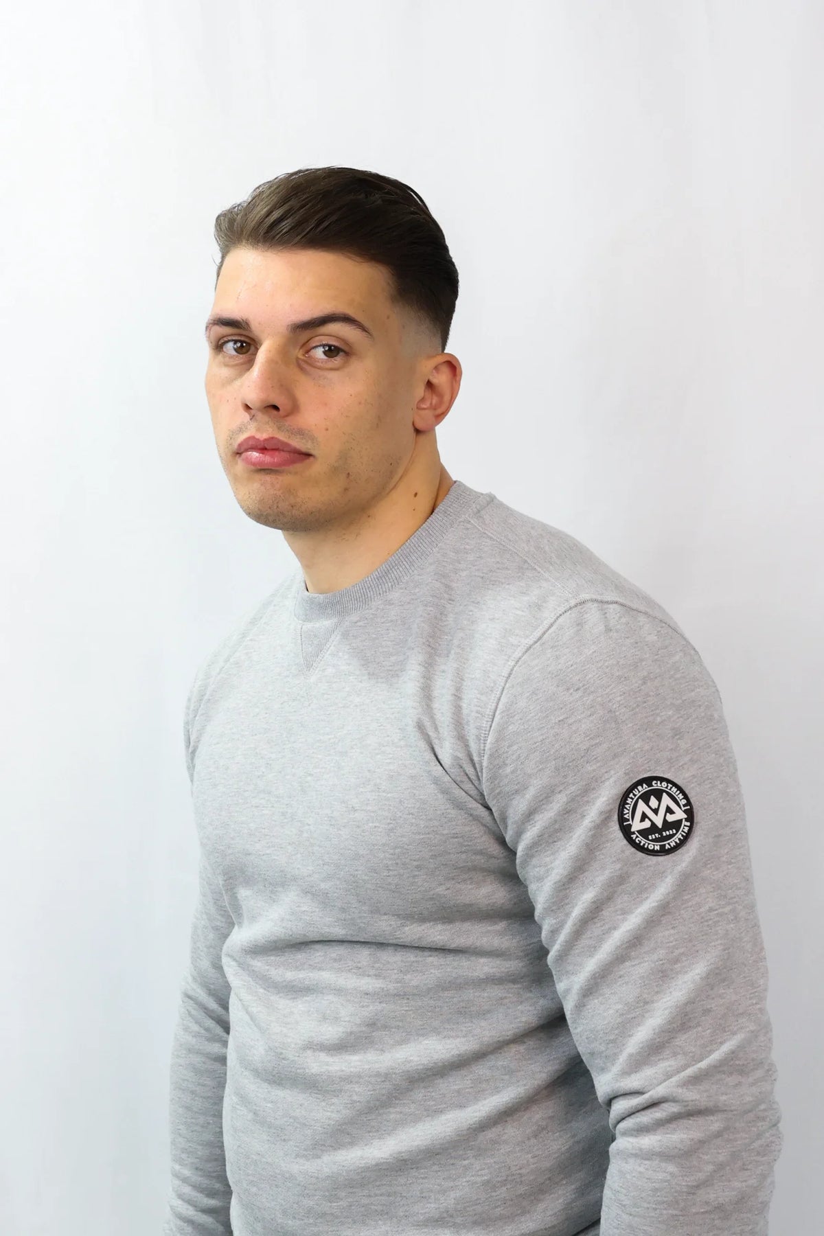 Light grey heathered crewneck sweatshirt with black patch logo on sleeve