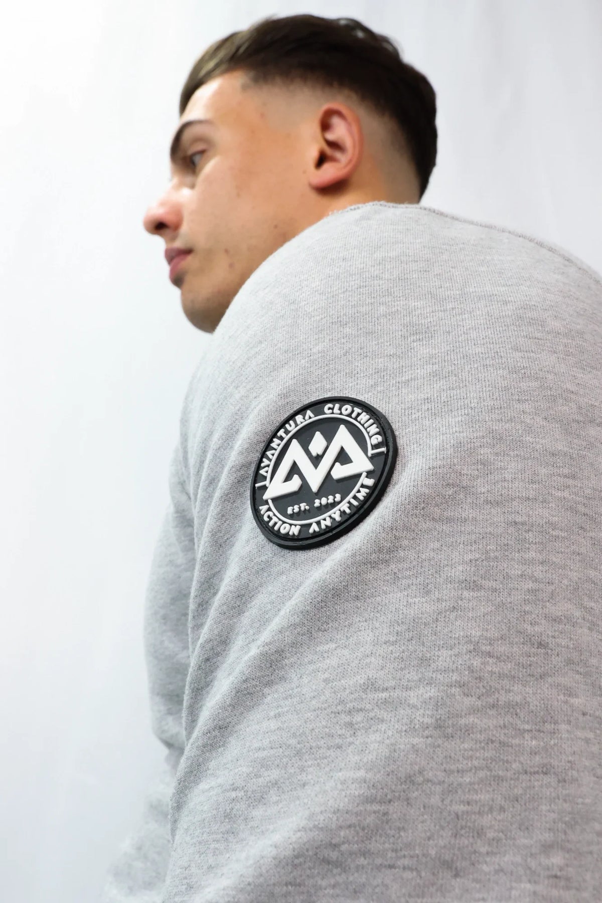 Back view of grey crewneck sweater showing left sleeve patch detail