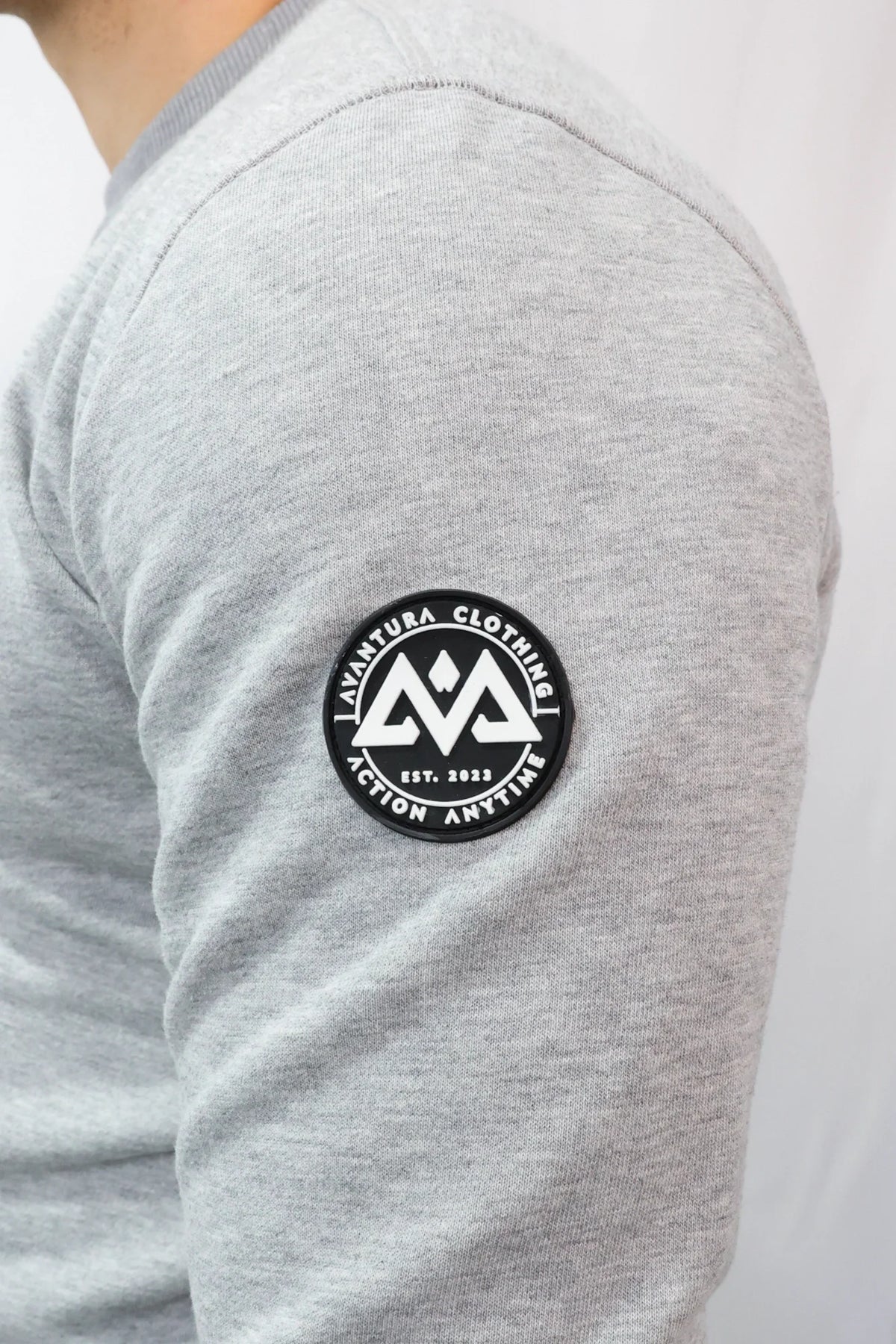 Close-up of rubberized 'Avantura Clothing' patch logo on grey sweatshirt