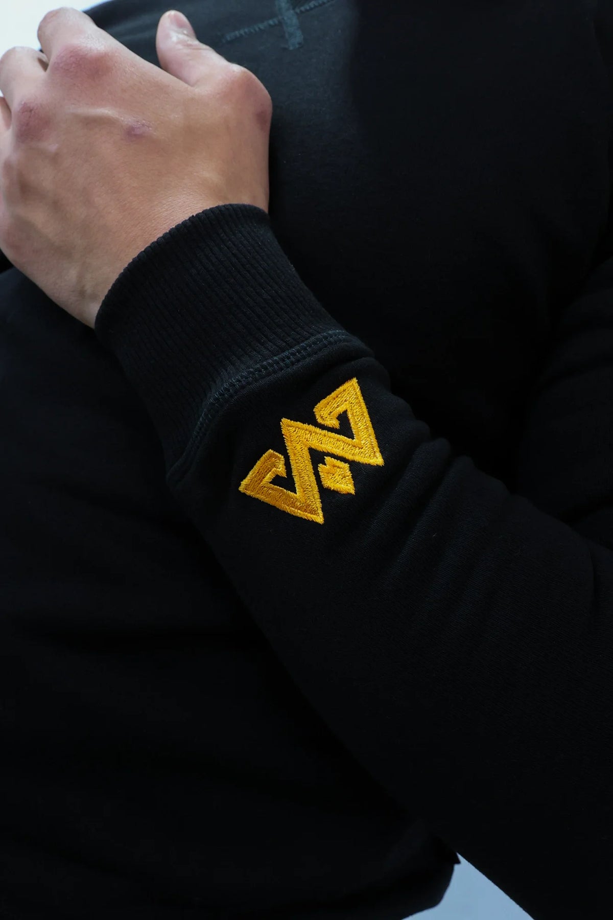 Black crewneck sweater with gold embroidered logo on left sleeve