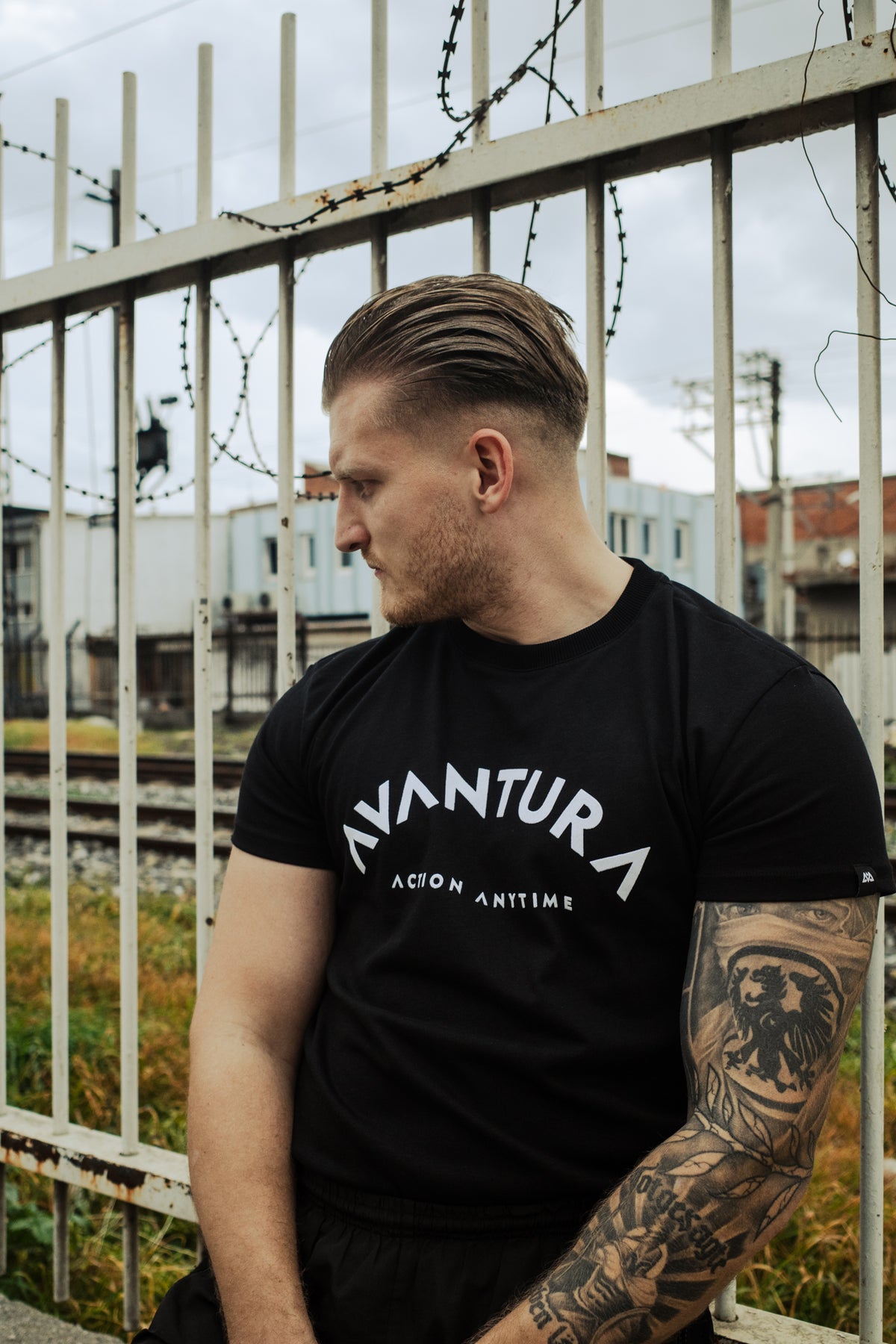 Side profile showing fit of black T-shirt with angular curved 'AVANTURA' chest graphic
