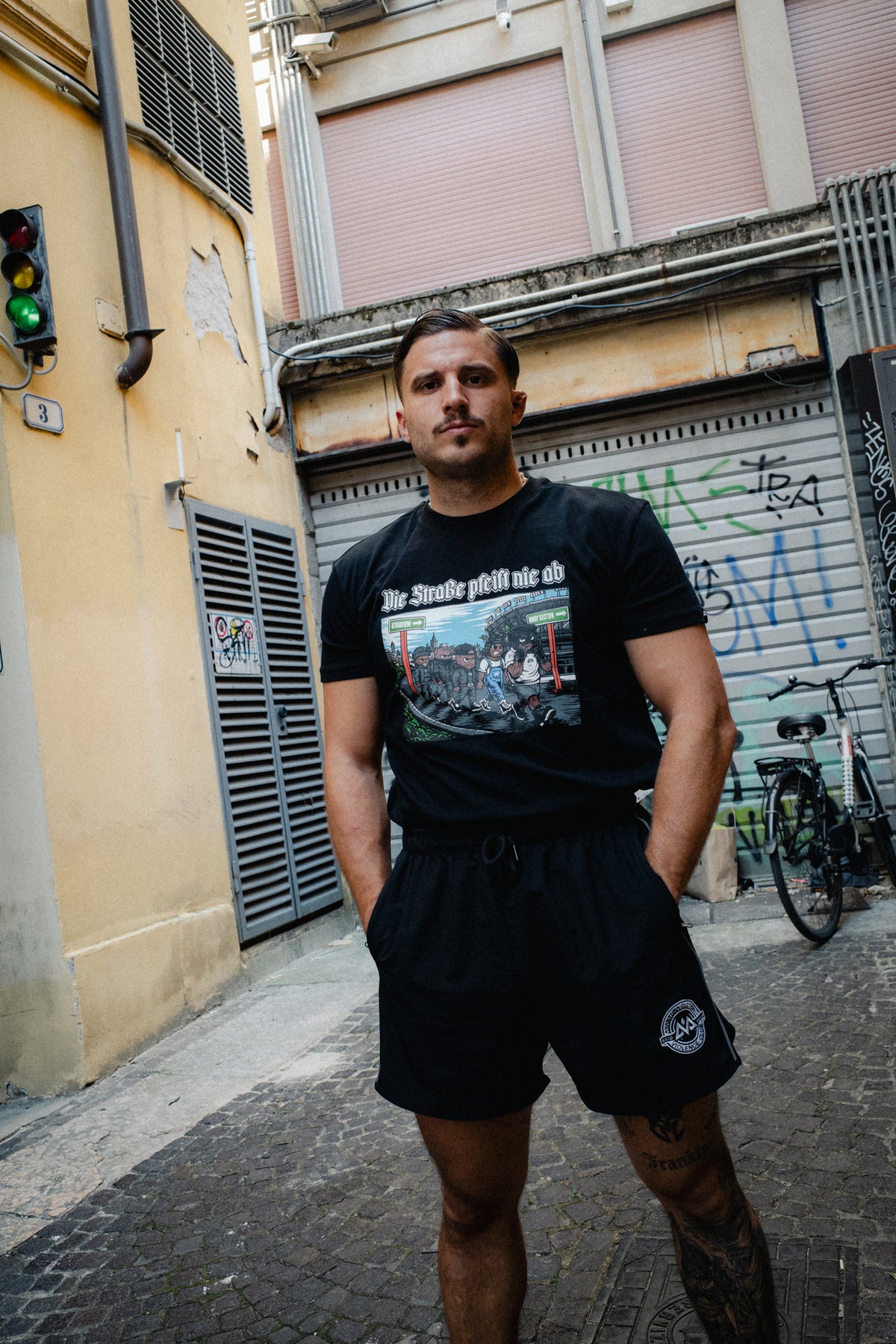 Man wearing black Die Straße pfeift nie ab T-shirt in urban alley