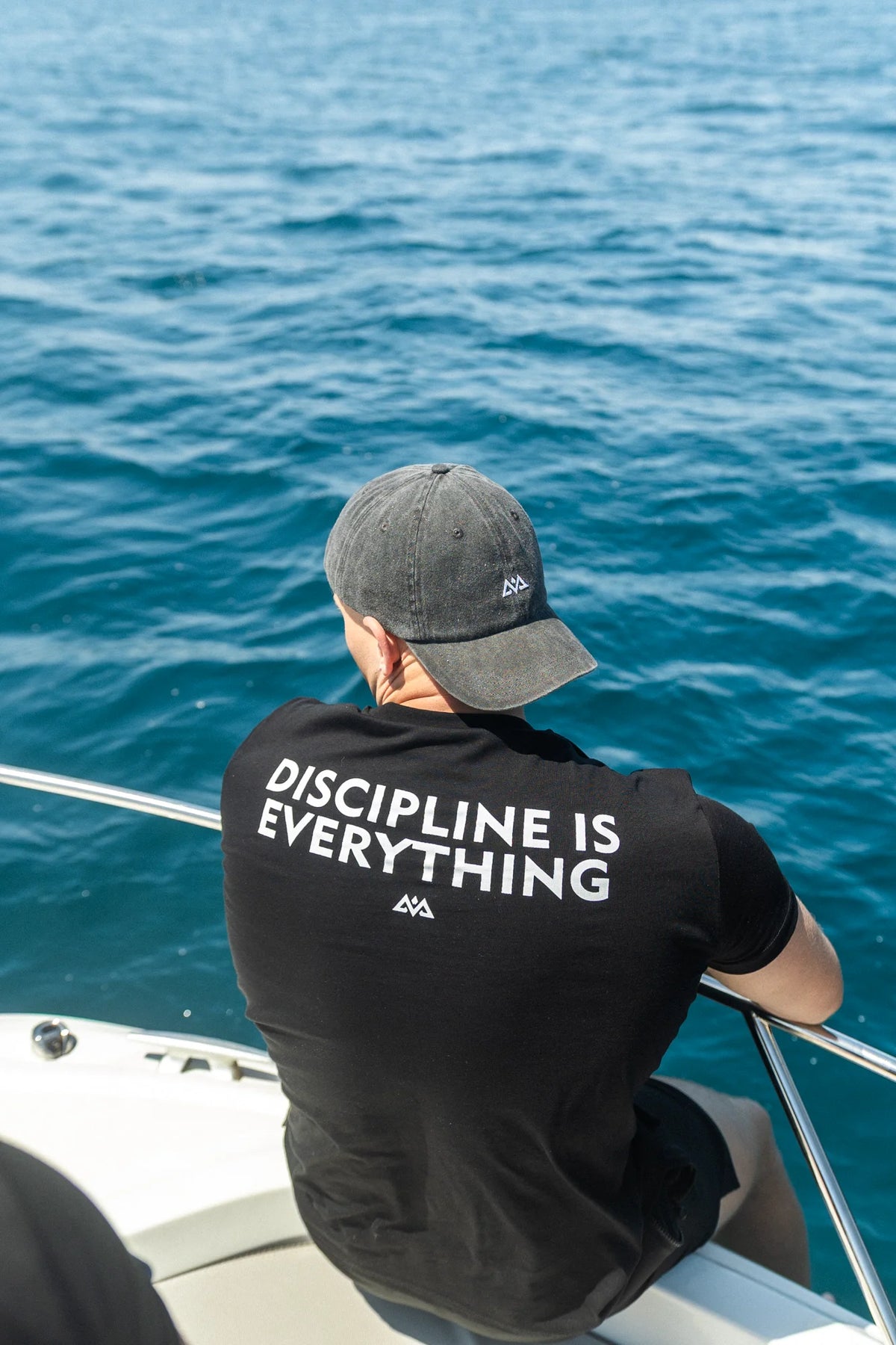 Man in black T-shirt with back print against blue water