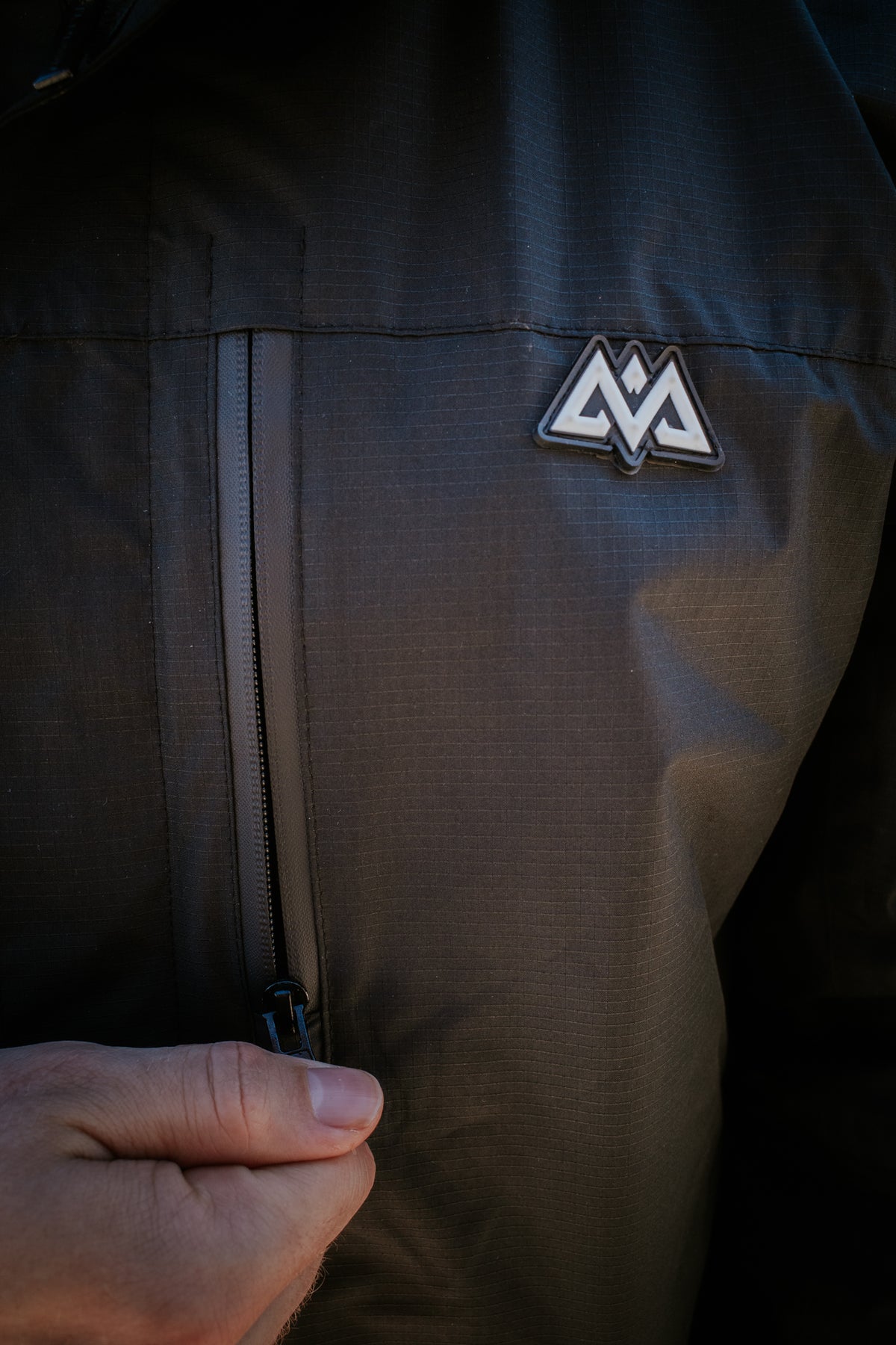 Close-up of rubber patch logo and zippered pocket on black ripstop jacket