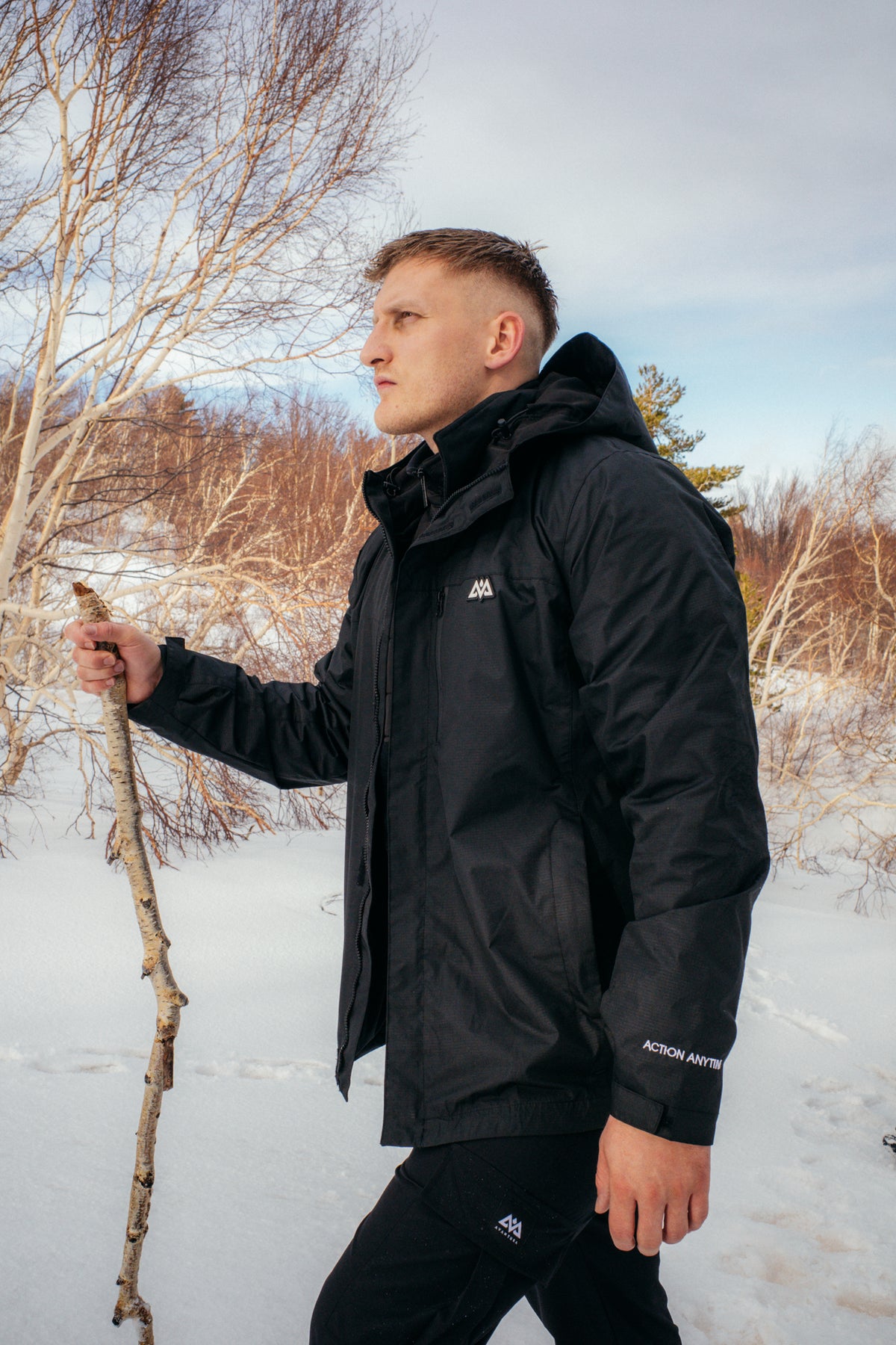 Side profile of black waterproof jacket with white chest logo in snow