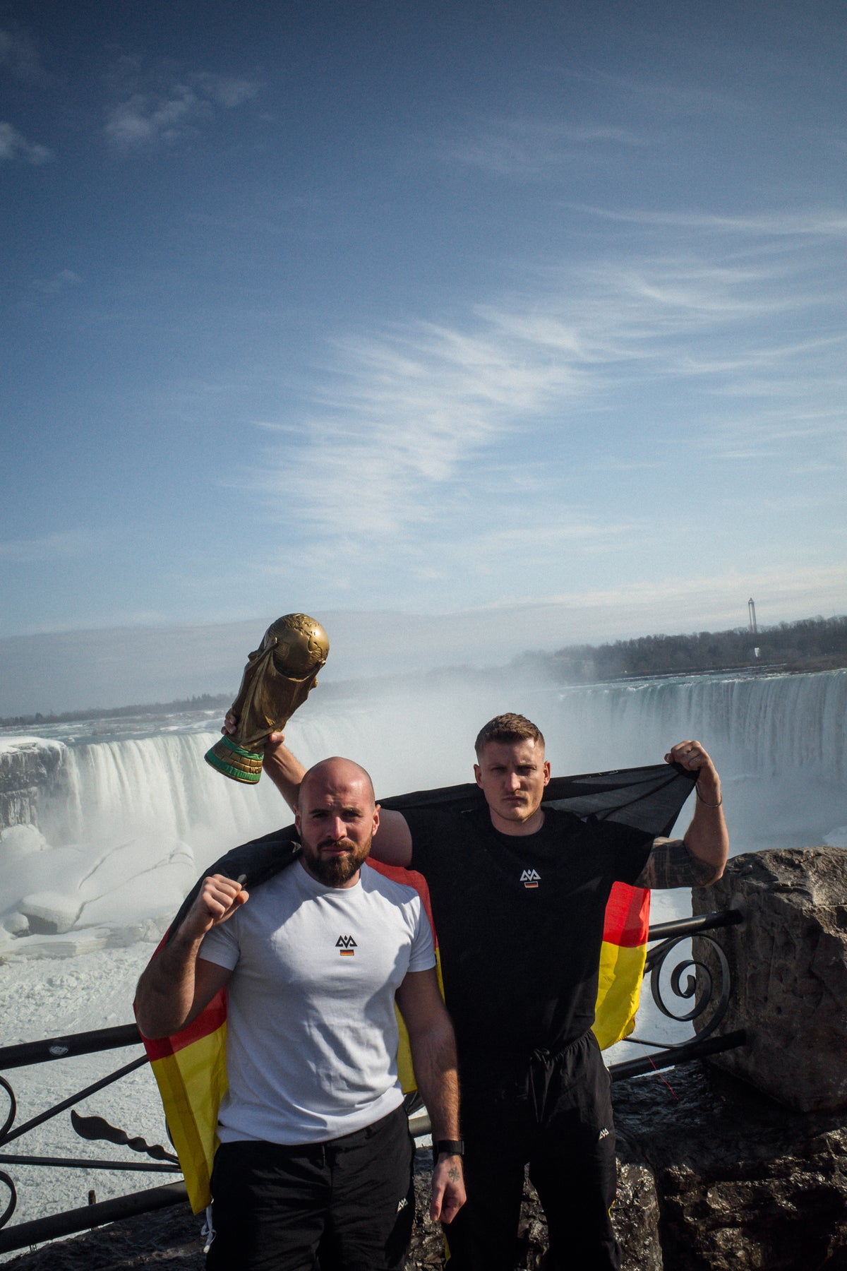Men posing at Niagara Falls with World Cup trophy and German flag T-shirts