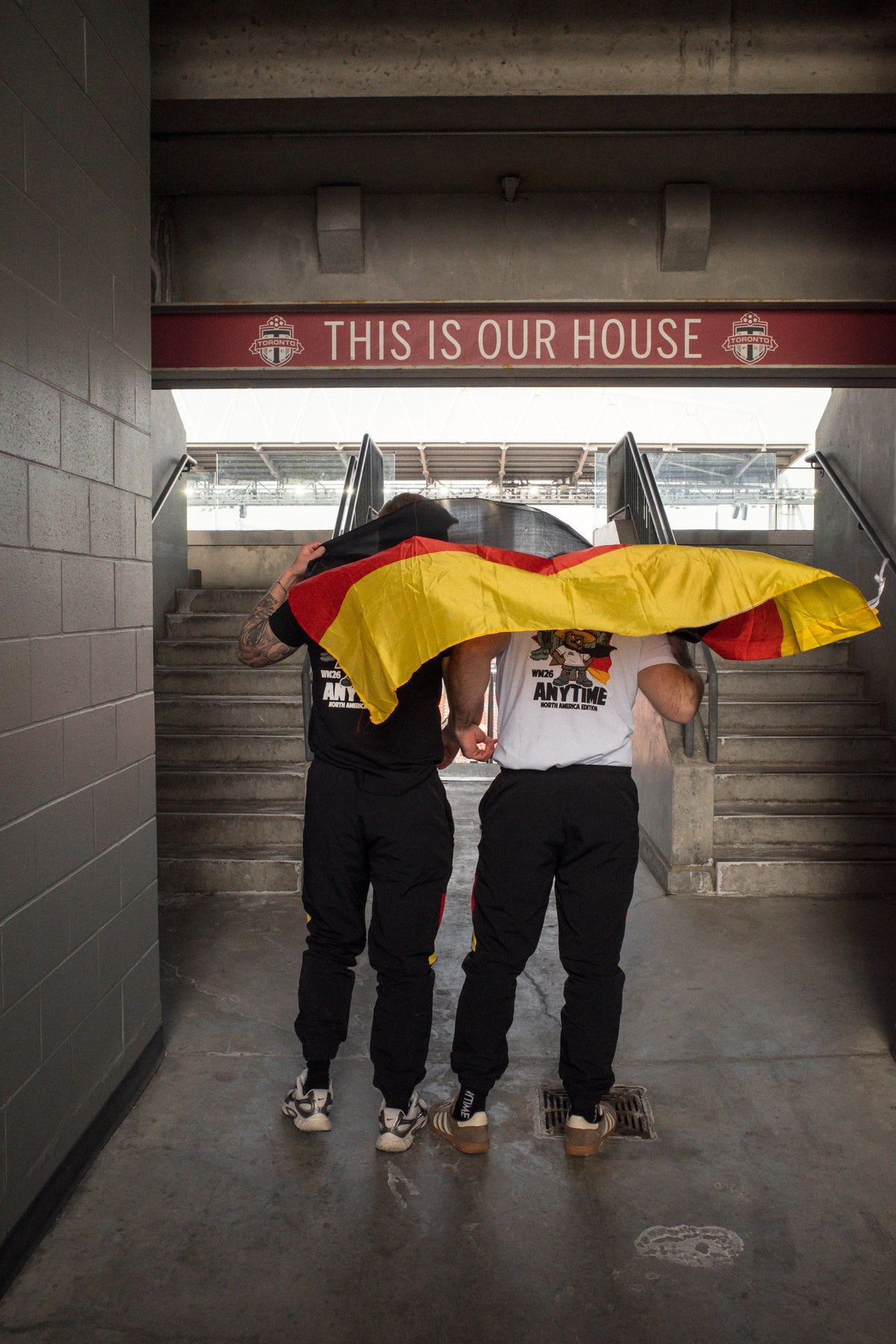 Männer im Stadiontunnel mit deutscher Flagge, weiße und schwarze T-Shirts sichtbar