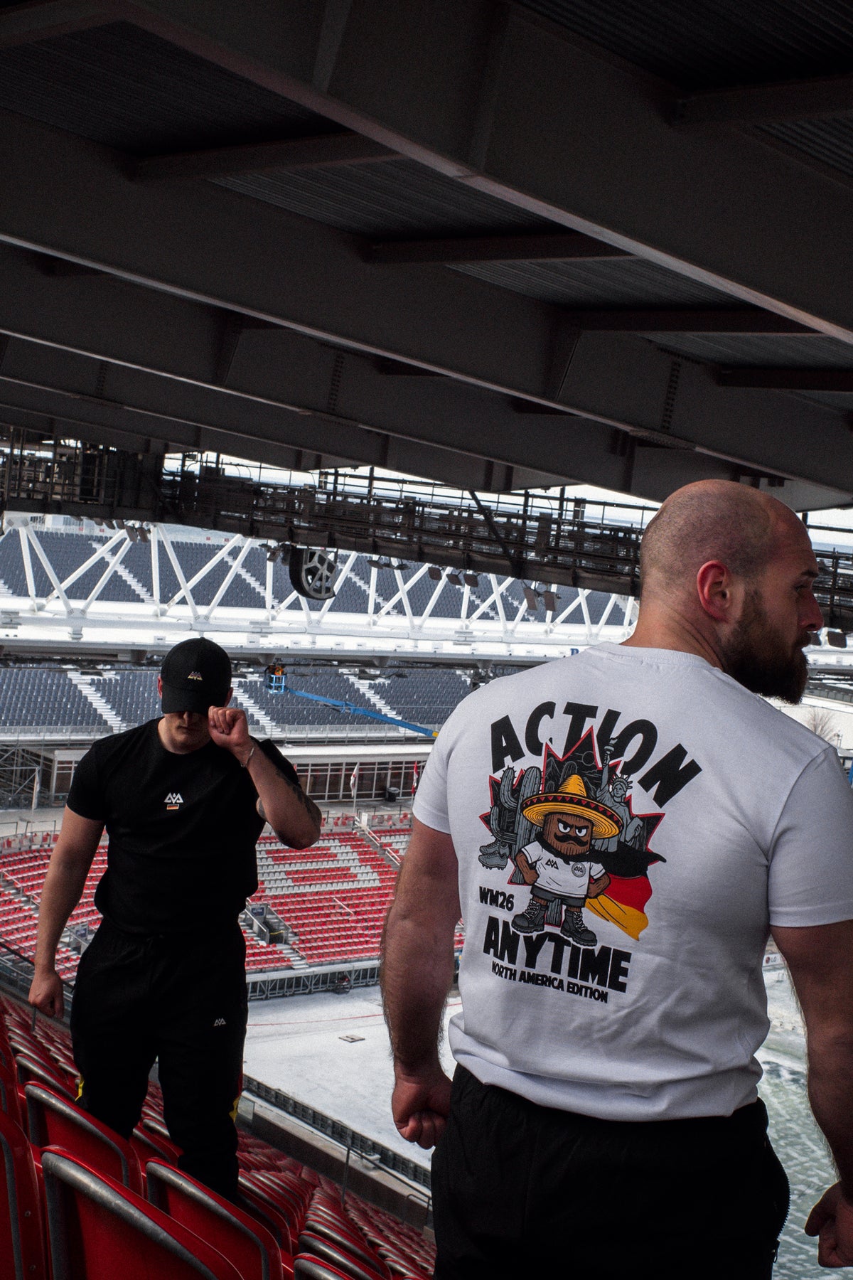 Profilansicht bärtiger Mann im weißen T-Shirt mit großem Rückenaufdruck auf Tribüne
