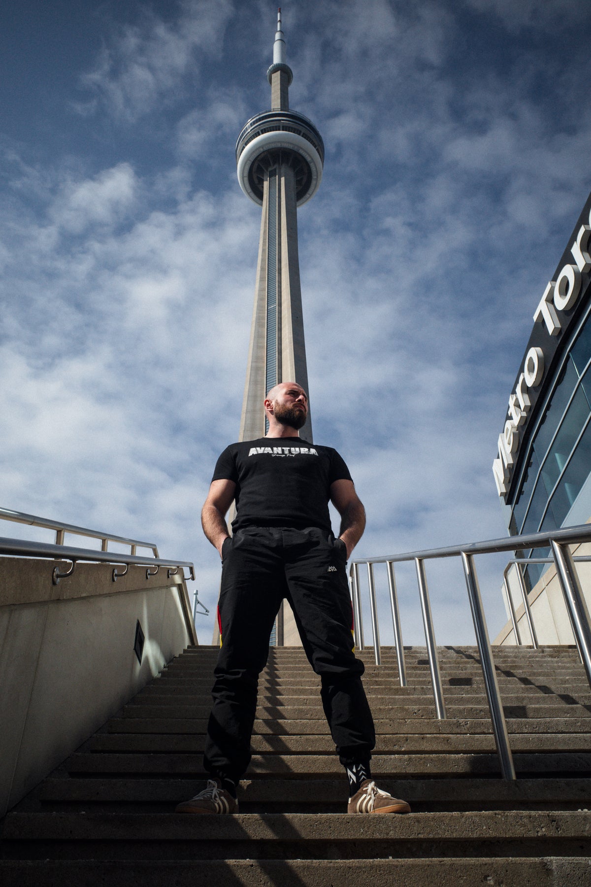 Ganzkörperansicht Avantura T-Shirt Schwarz auf Außentreppe vor CN Tower