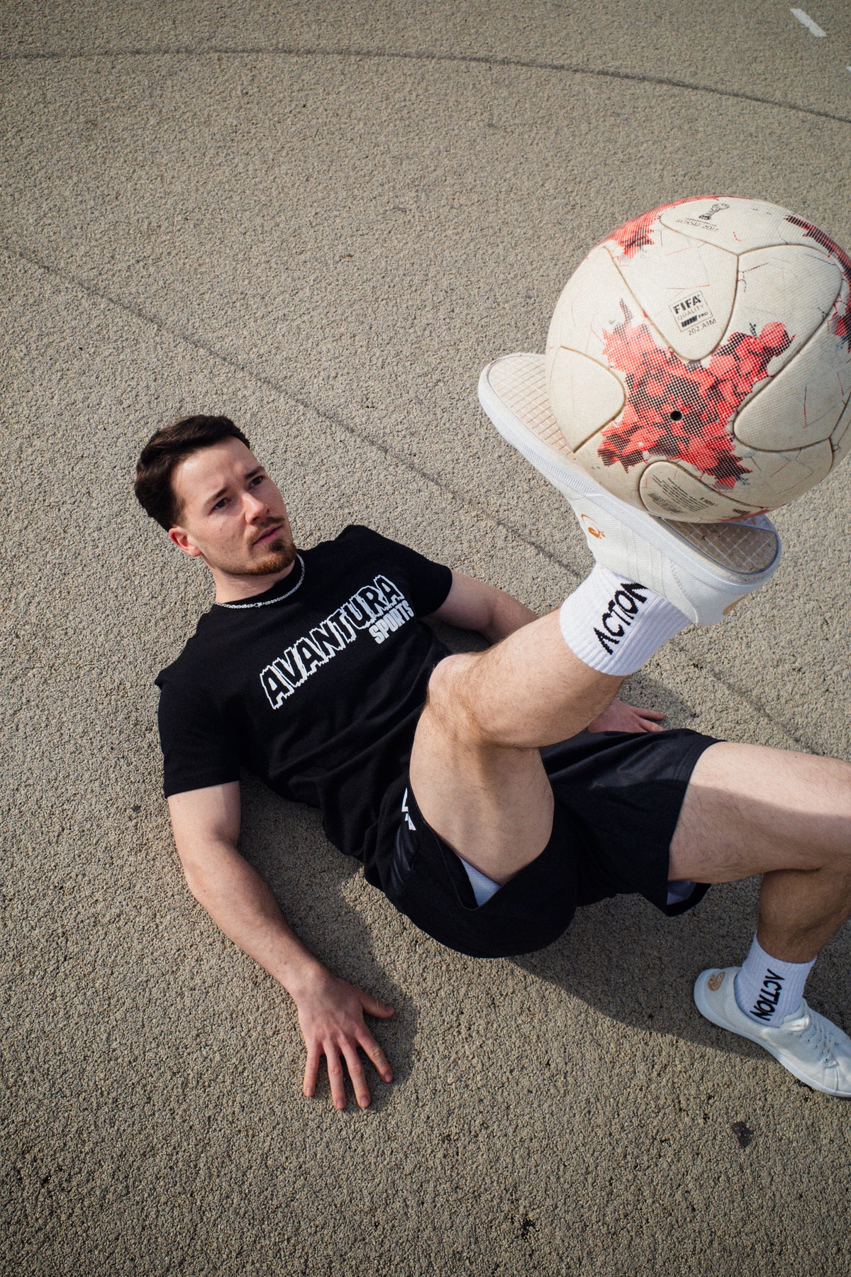Man balancing soccer ball wearing black Avantaura Sports graphic T-shirt