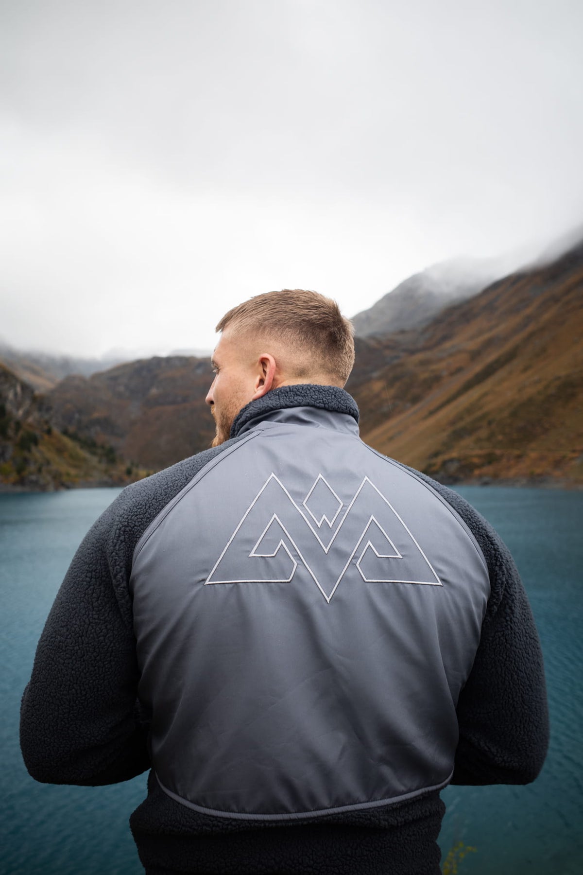 Rückansicht der grauen Fleecejacke mit weiß umrandetem geometrischem Logo