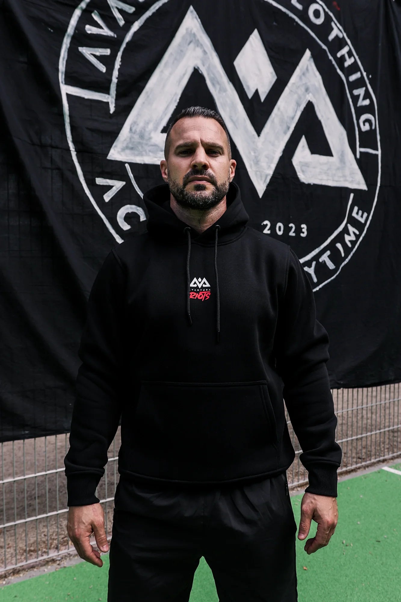 Man wearing black Avantura hoodie with kangaroo pocket and chest logo against branded banner