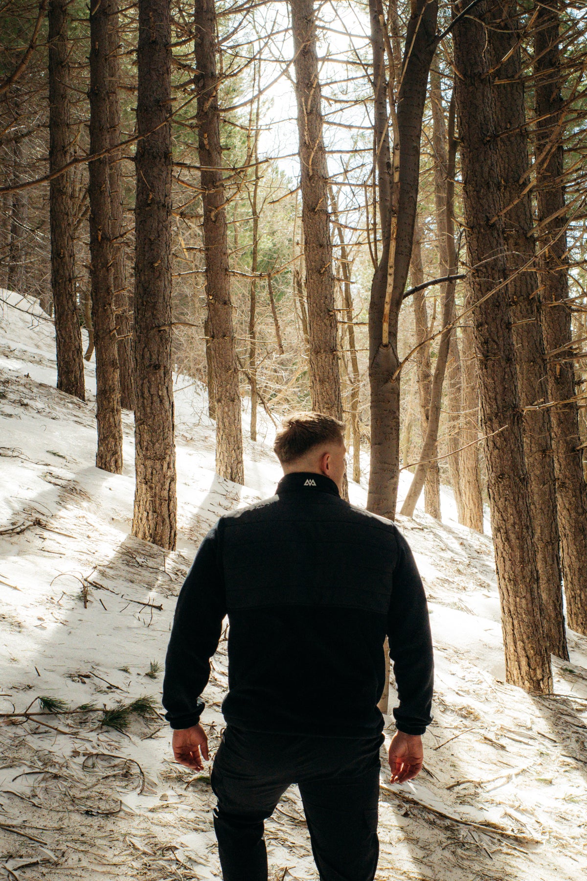 Black insulated fleece jacket with horizontal quilting and rubber patch logo, worn in snowy forest
