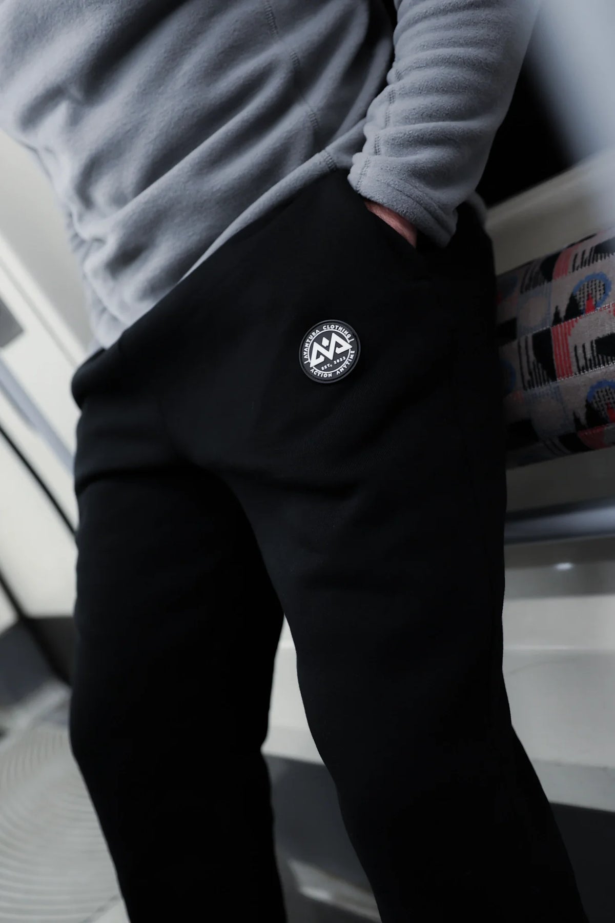 Waist and thigh detail of black joggers featuring stitched rubber brand logo patch