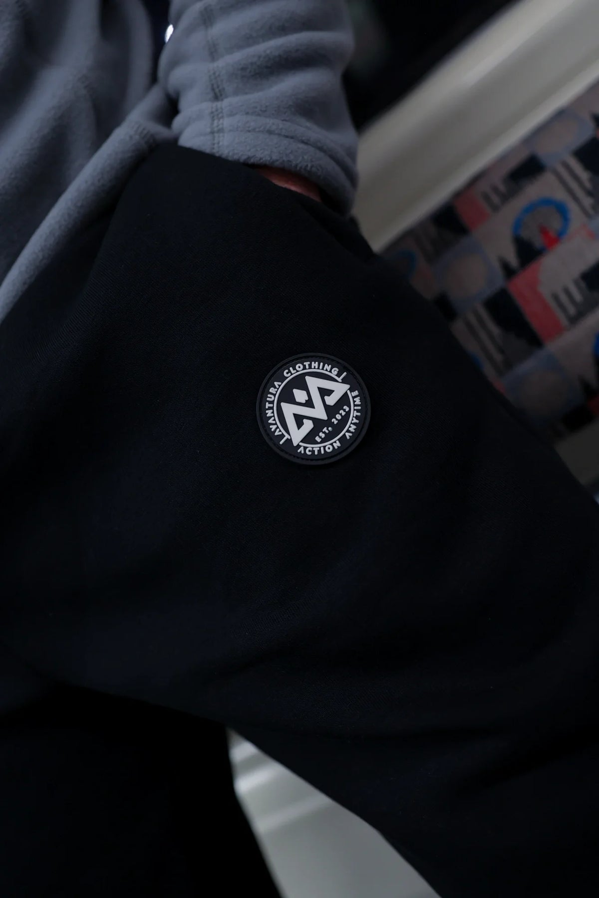 Black jogger pants detail showing embroidered rubber patch logo with white geometric symbol