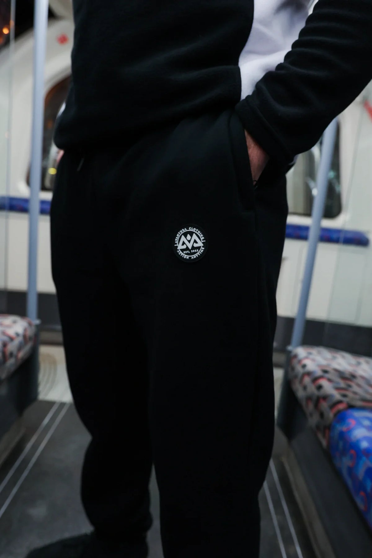 Close-up of black jogger side pocket and raised circular logo patch on left thigh