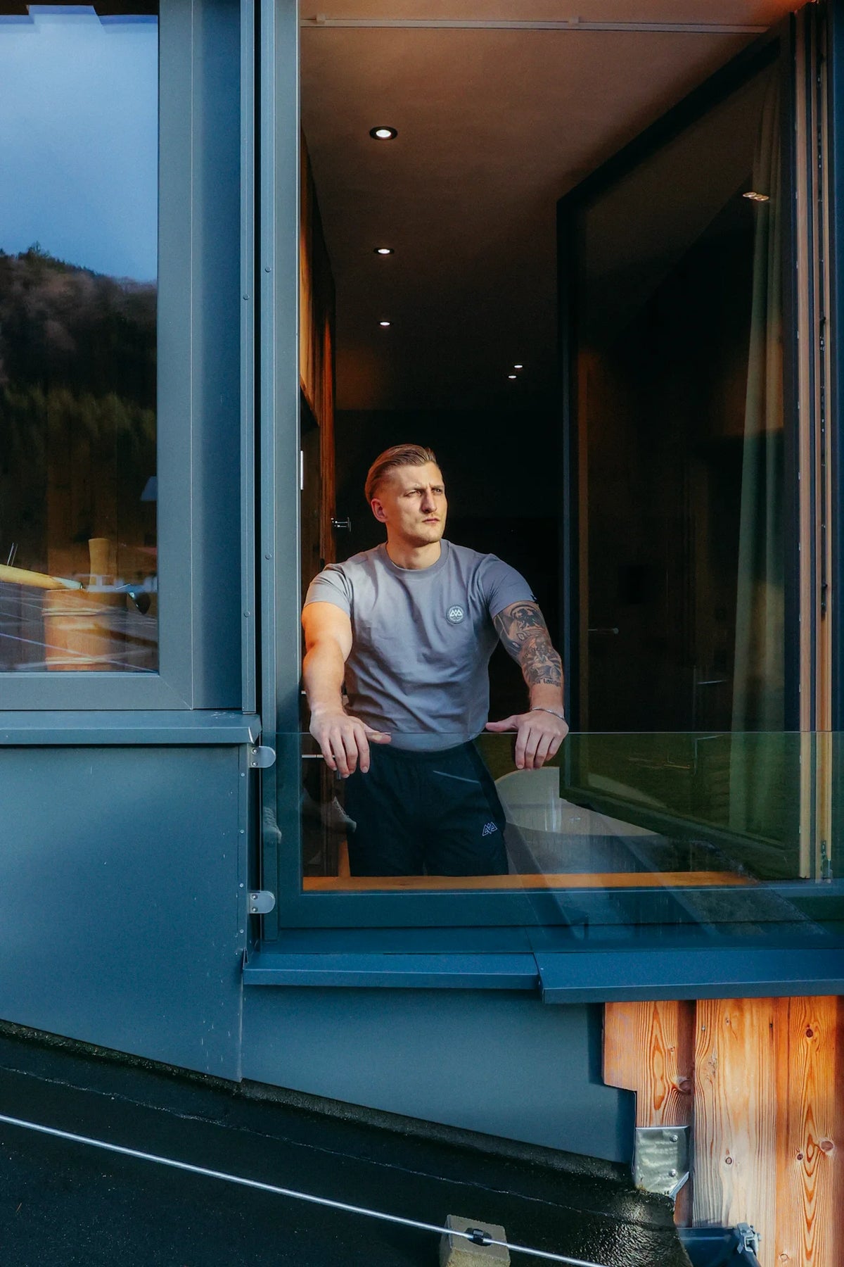 Grey lifestyle-fit T-shirt worn by a tattooed man on a glass railing