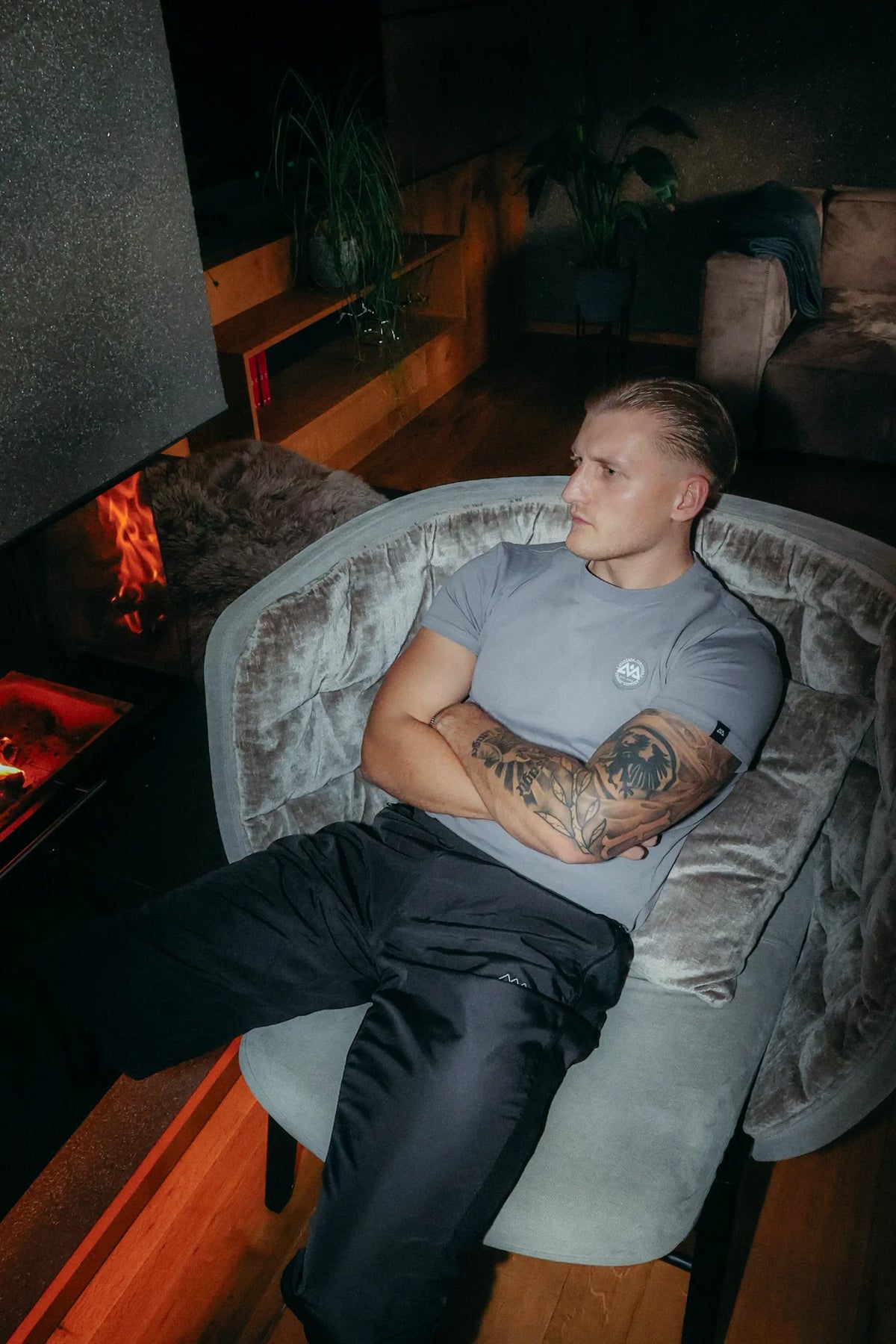 Grey T-shirt with sleeve label and chest logo, sitting relaxed in a velvet chair
