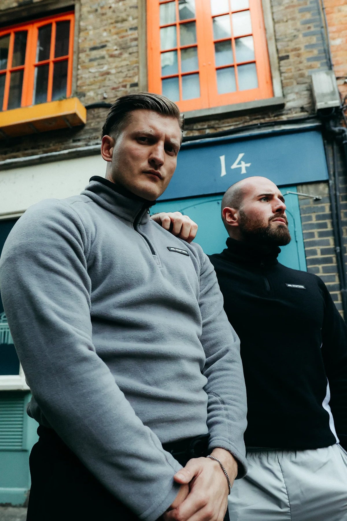Two men modeling grey and black halfzip fleece sweaters outdoors, showing color variants