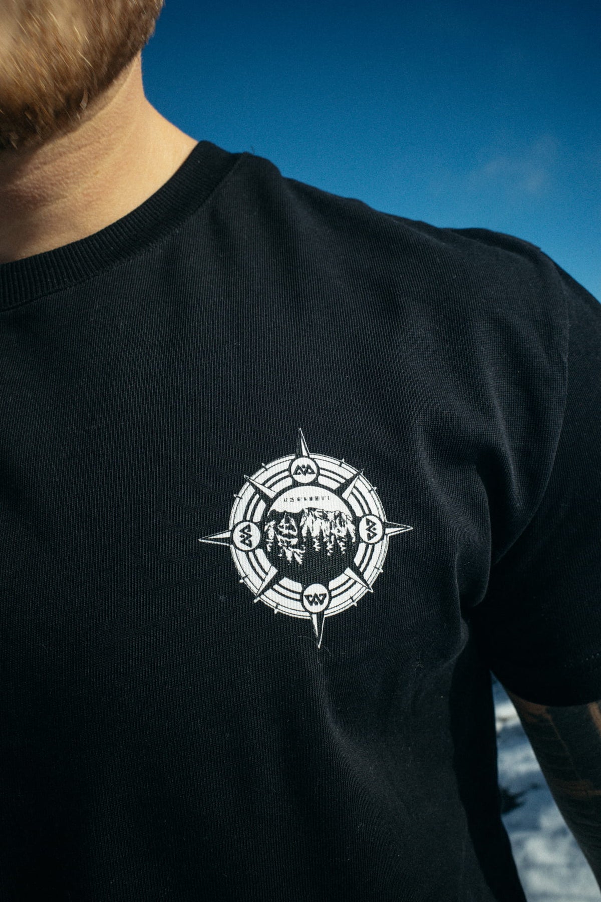 Close-up black T-shirt with white compass logo on left chest