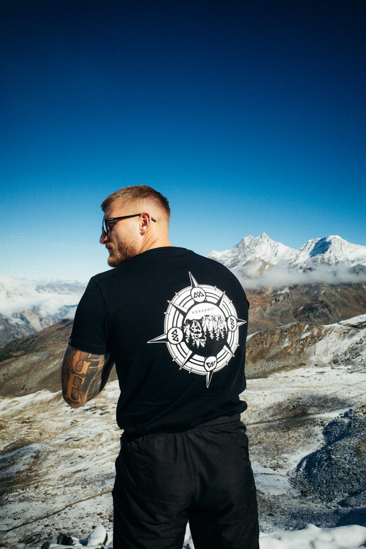 Black T-shirt with large compass back print worn on snow-covered mountains