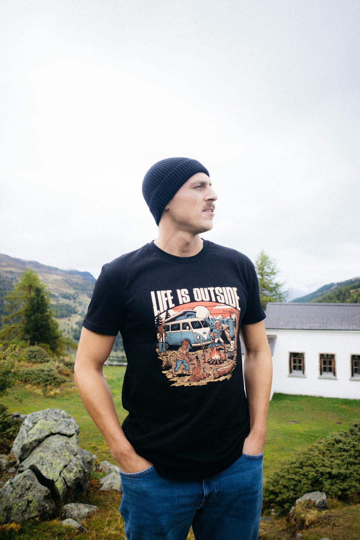 Mann trägt schwarzes LIFE IS OUTSIDE T-Shirt vor weißem Haus