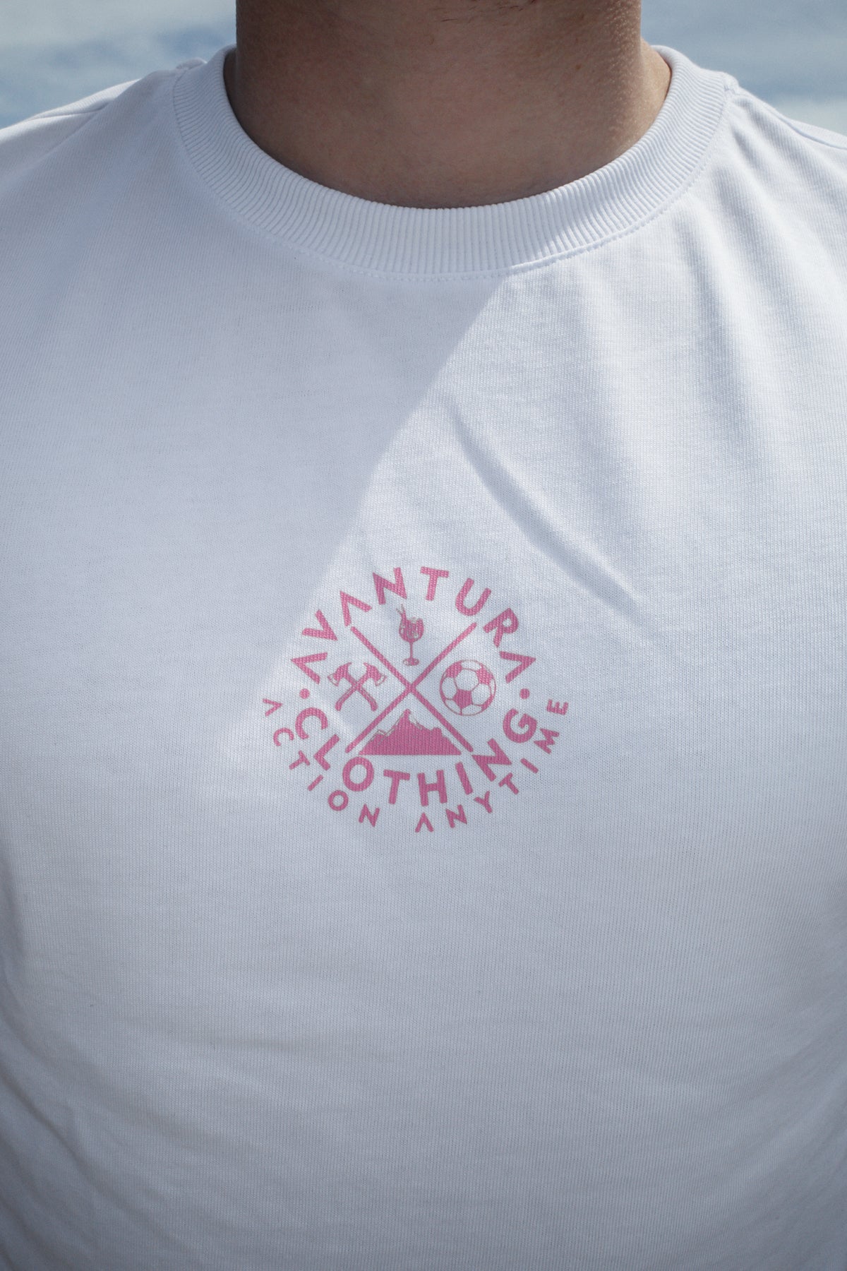 Close-up of white t-shirt chest showing pink circular logo and ribbed collar detail