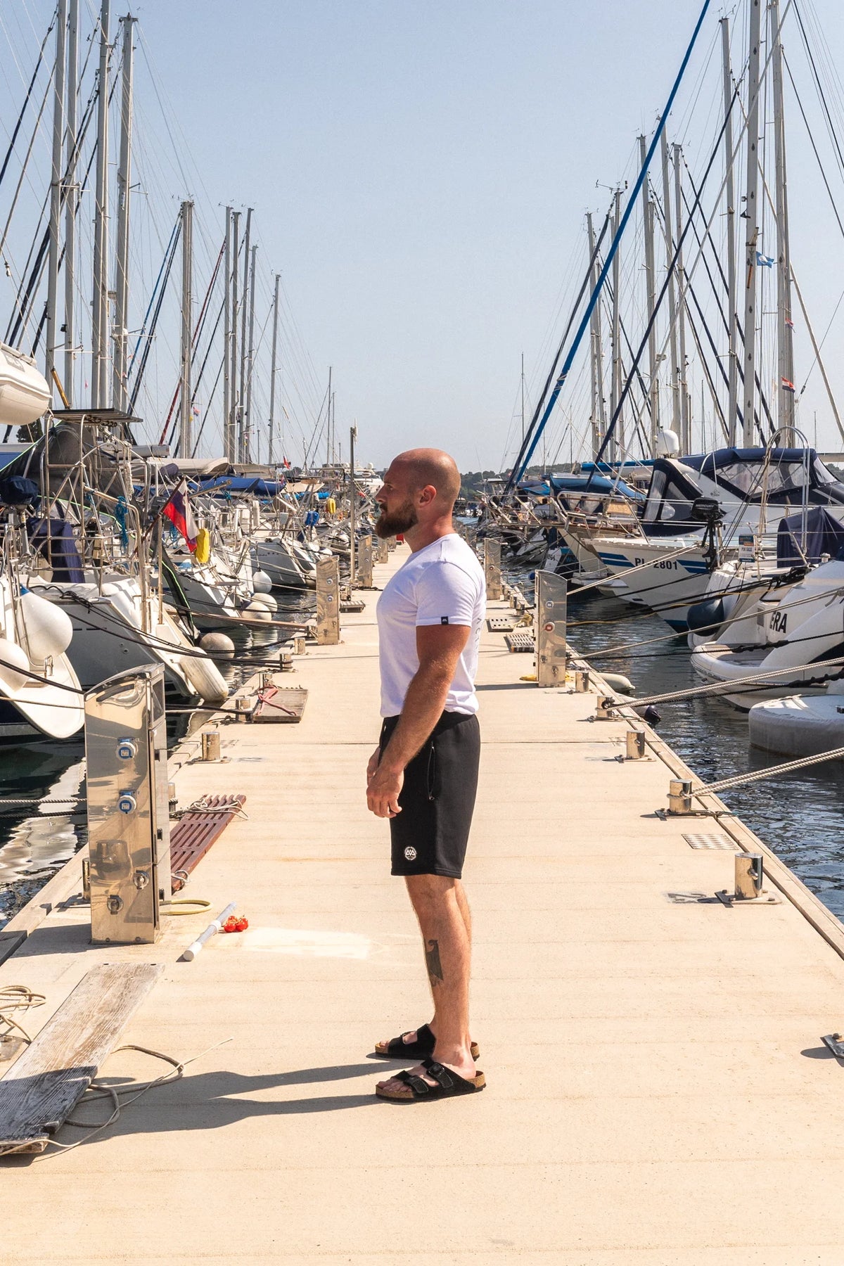Side profile fit of white t-shirt with chest logo and sleeve tag at marina