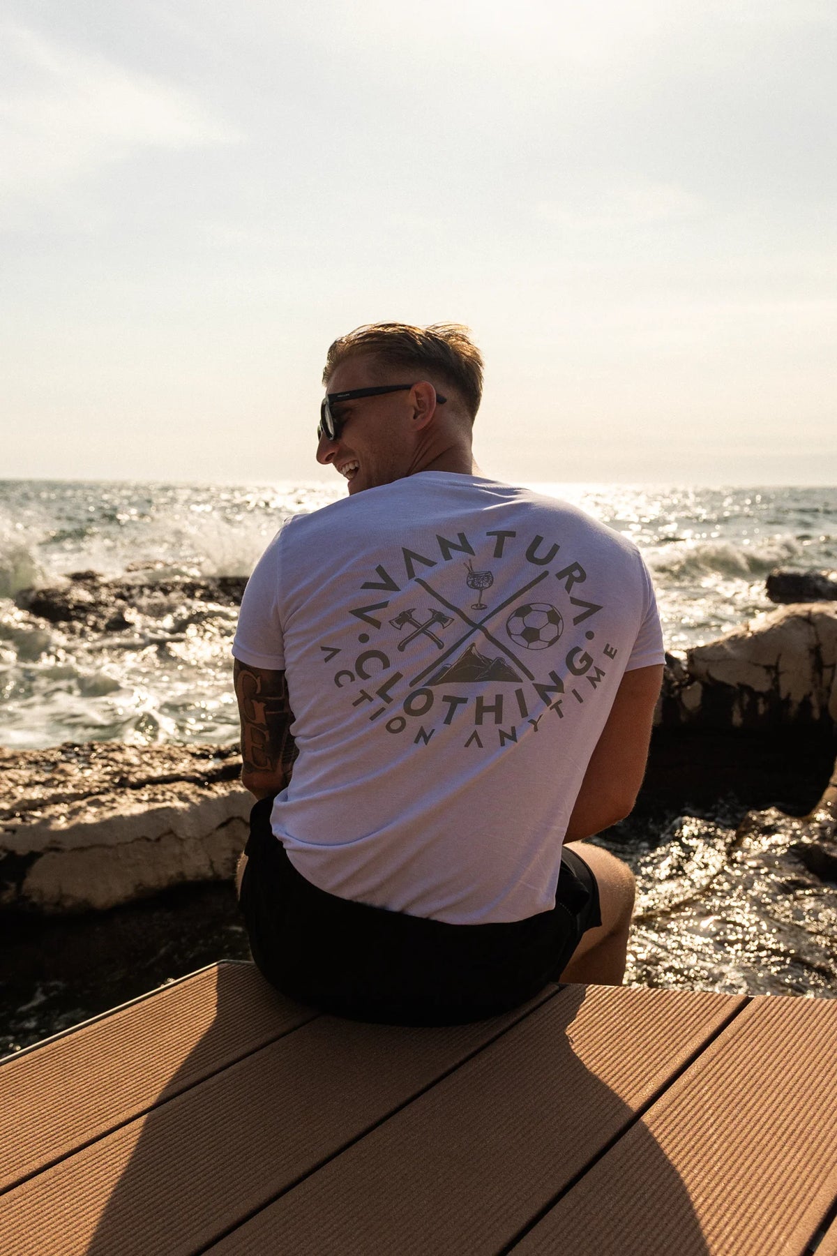 Man wearing white t-shirt with back logo print sitting on dock by ocean